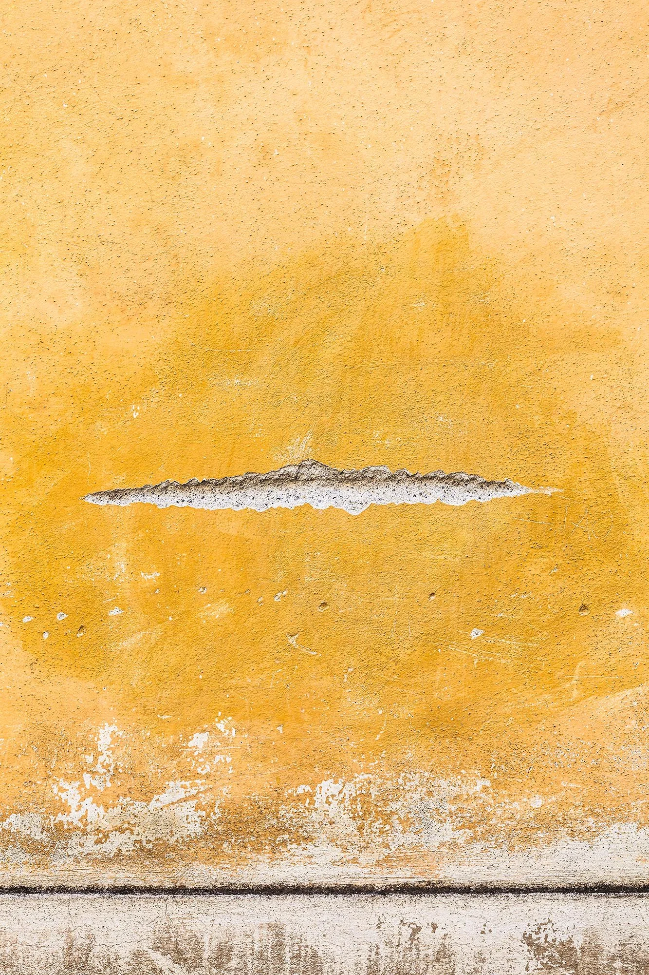 Close-up di pareti di diversi colori con vernice sbucciata e crepe, da sopra a sotto: giallo ocra, beige e grigio scuro.