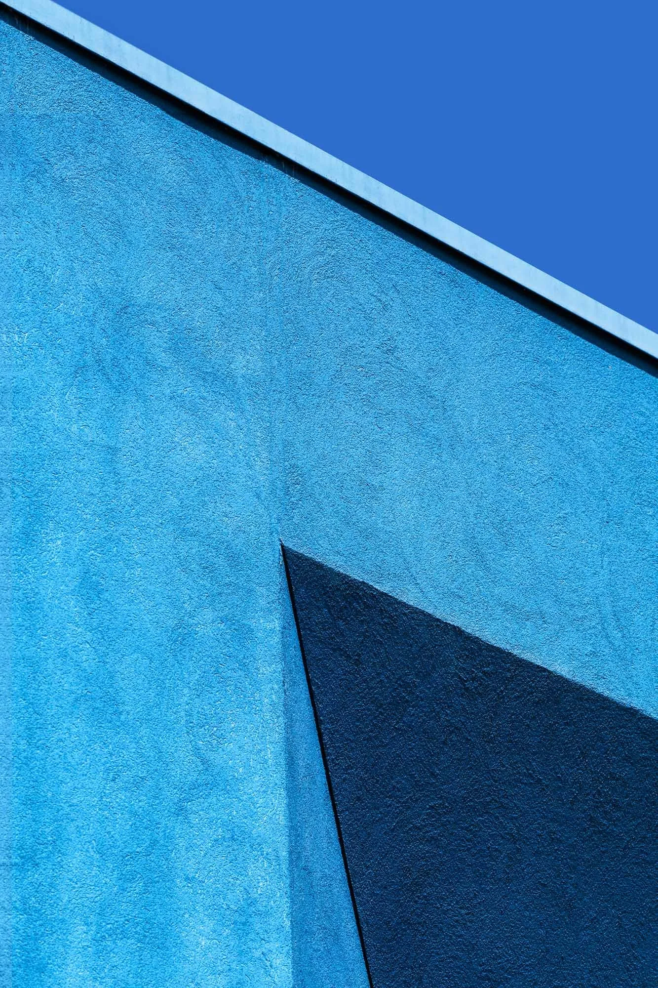 Dettaglio di facciata di un edificio con pareti di colore blu e una linea diagonale che separa due tonalità di blu.