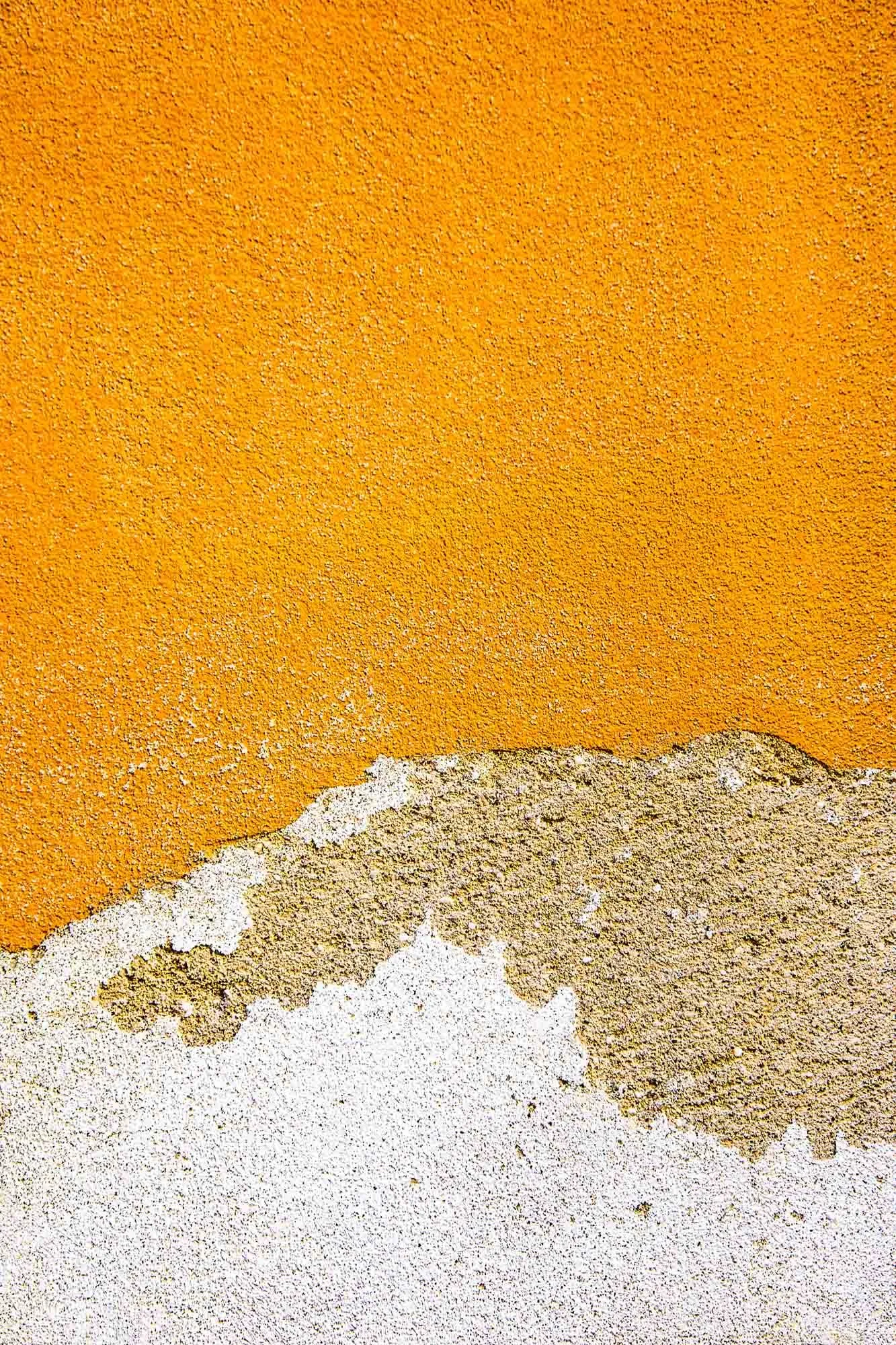 Immagine di una parete con intonaco di vari strati di vernice in vari colori e texture, con alcune parti in stucco grigio e bianco.
