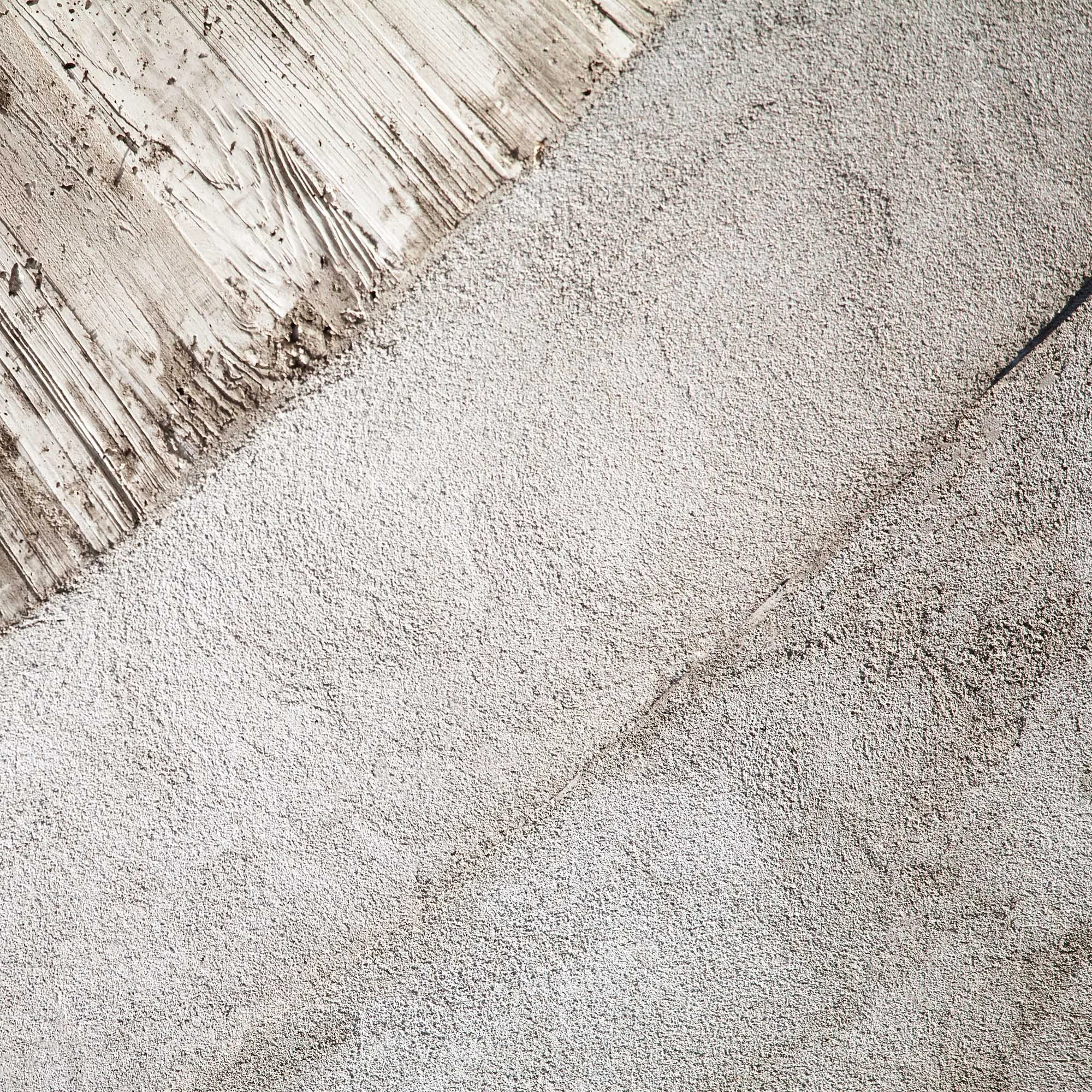 Primer piano di una parete in cemento con una zona di stucco bianco che si sta costruendo.