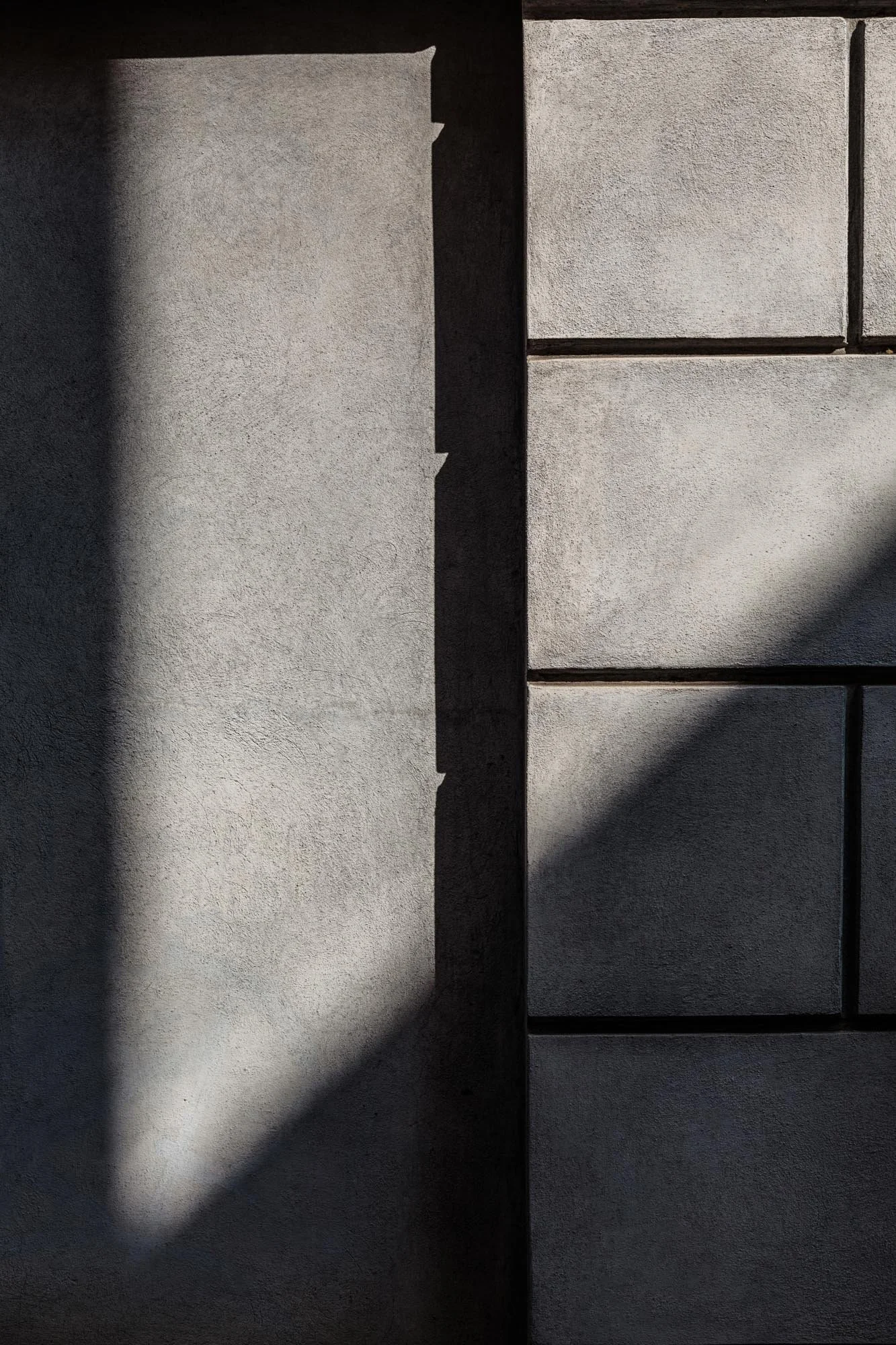 Particolare di una parete in cemento con zone d'ombra e linee di divisione.