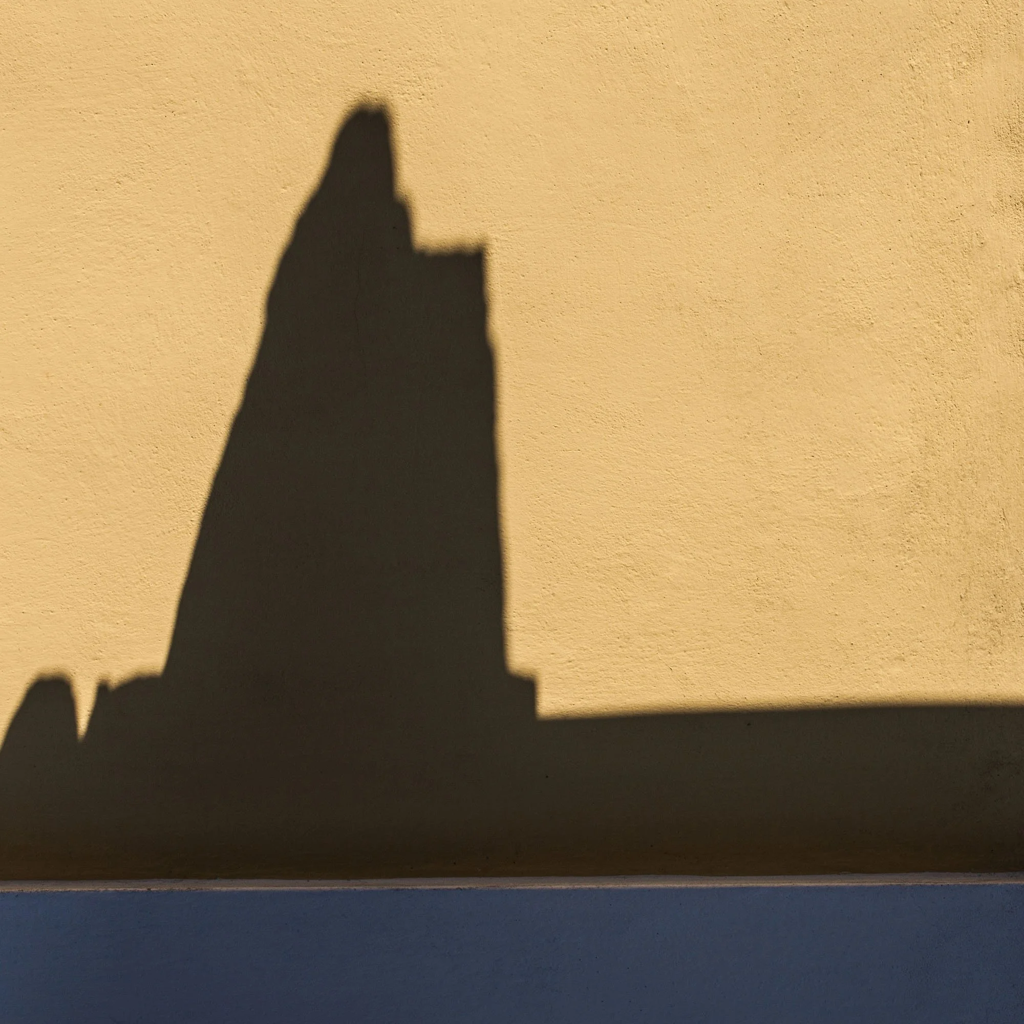 Ombra di un edificio con un tetto a punta e una punta più alta, proiettata sul muro giallo.