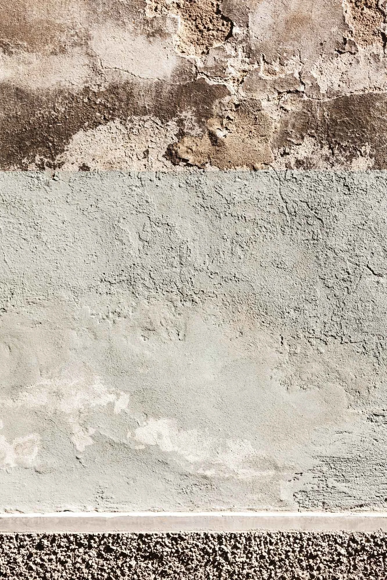 Immagine di una parete con diversi strati di intonaco e finitura nei toni del grigio e del marrone