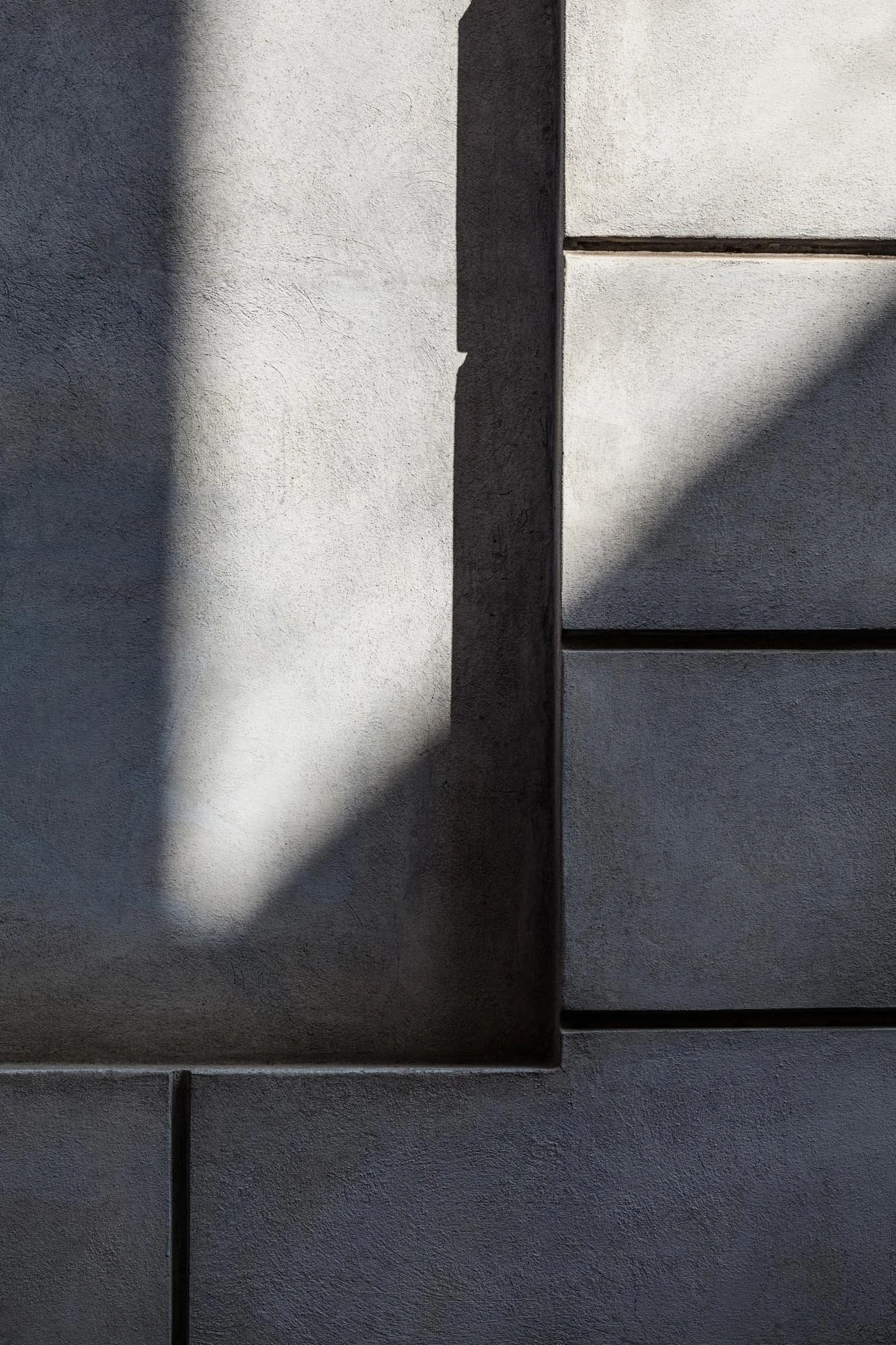 Una parete di cemento con linee di divisione e ombre che creano contrasti di luci e ombre