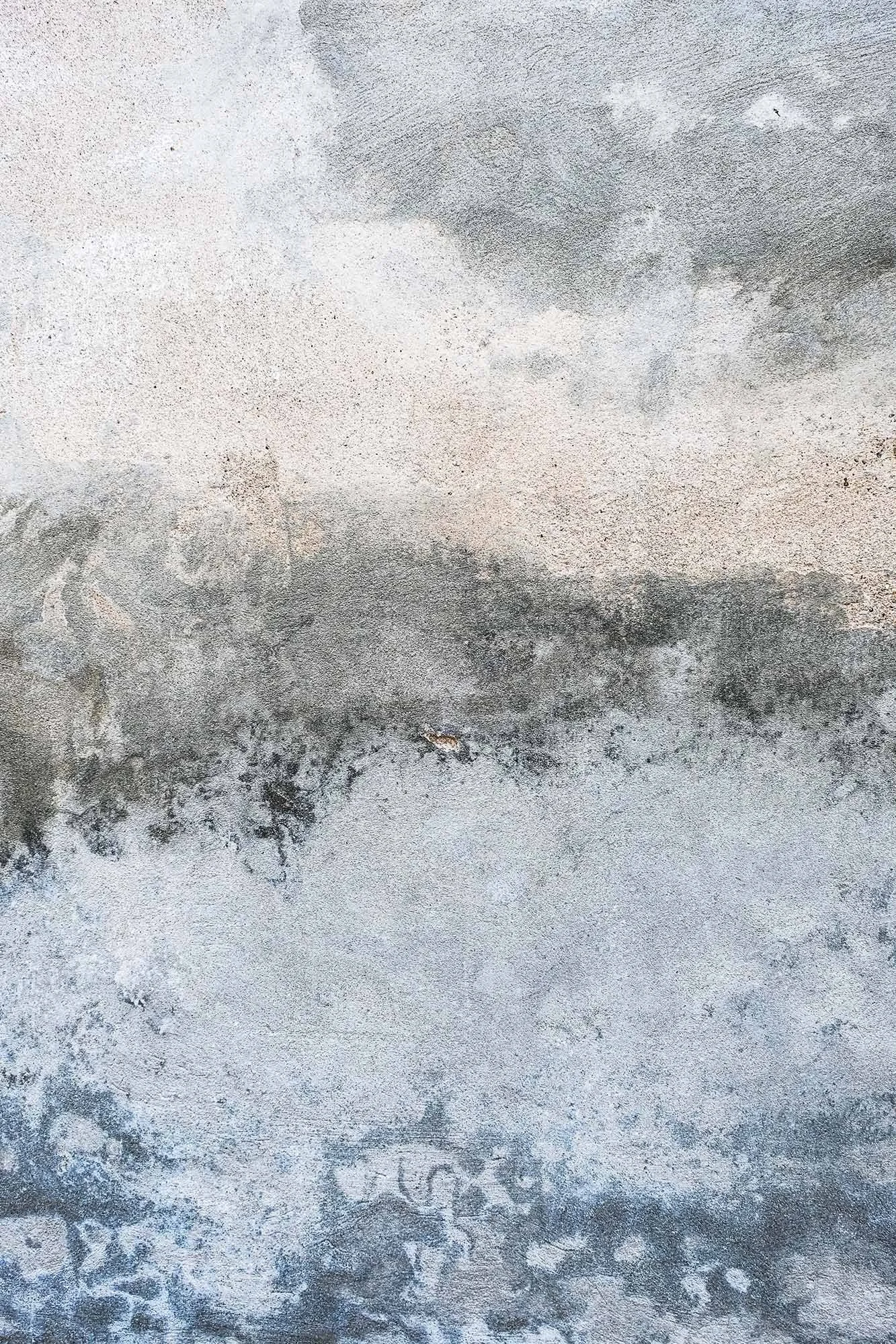 Superficie di un muro con effetti di scolorimento e tracce di colore grigio, nero e bianco.