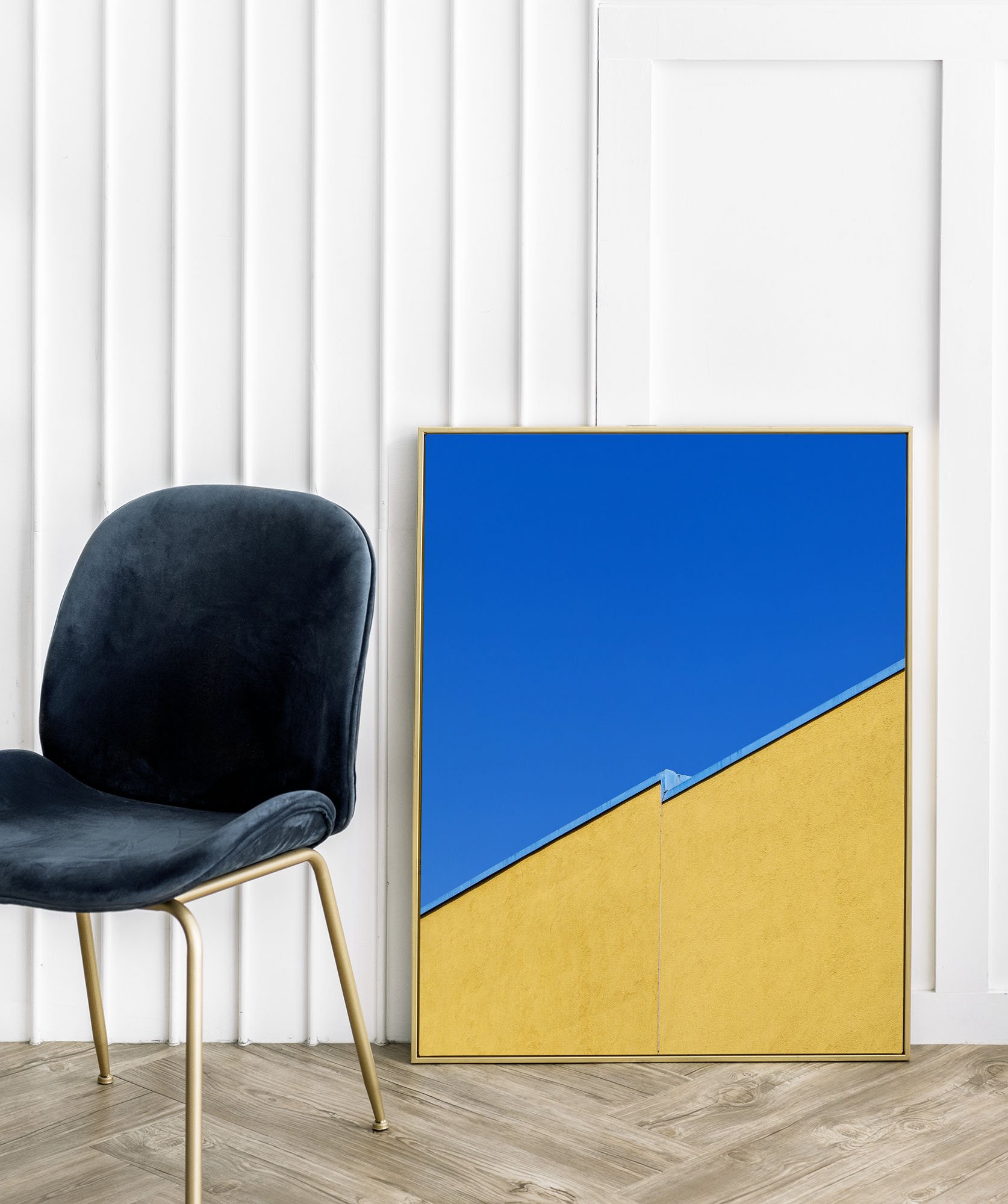 Sedia nera con gambe dorate, quadro astratto con una composizione geometrica blu e gialla, in un ambiente interno con pareti bianche e pavimento in legno.