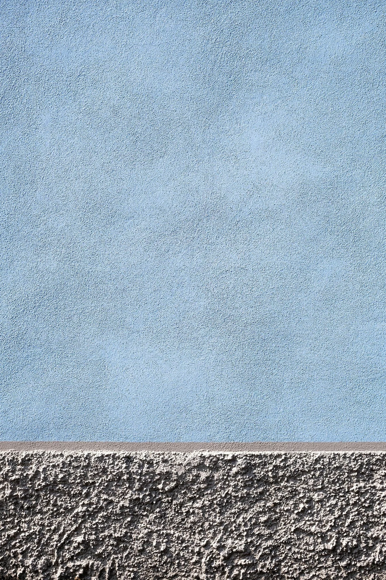 Prima sezione di vero muro colorato di azzurro con superficie liscia. Seconda sezione di muro di finitura ruvida di colore grigio scuro.