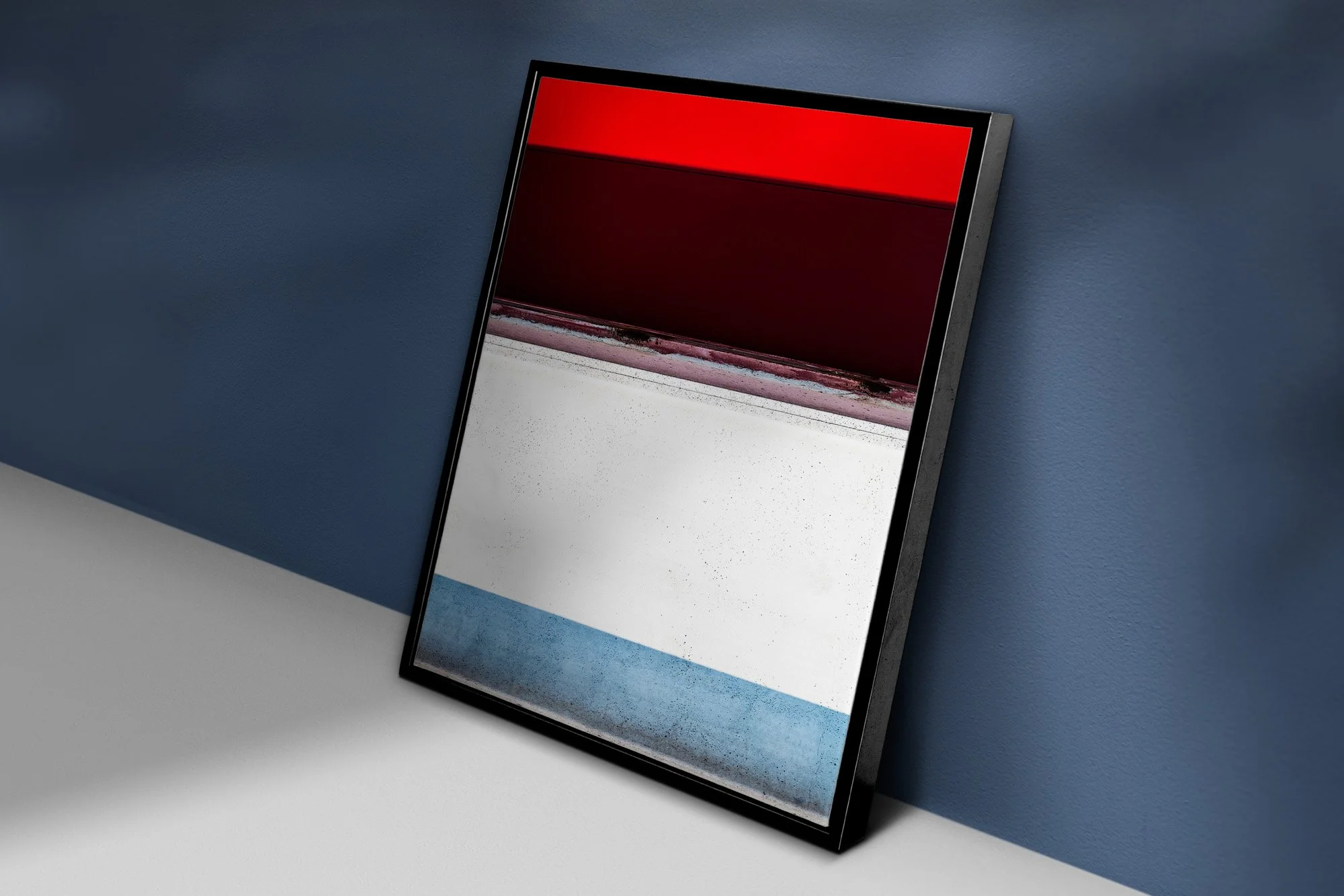 Un quadro astratto composto da linee rosse, nere, bianche e blu, appoggiato in terra davanti ad una parete blu.