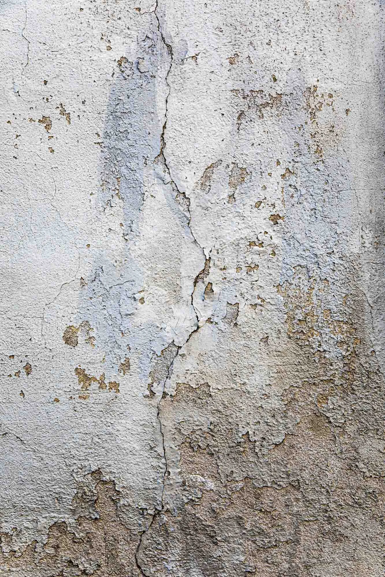 Muro di parete con vernice bianca sbiadita e vernice che si screpola, evidenziando crepe e zone di deterioramento.