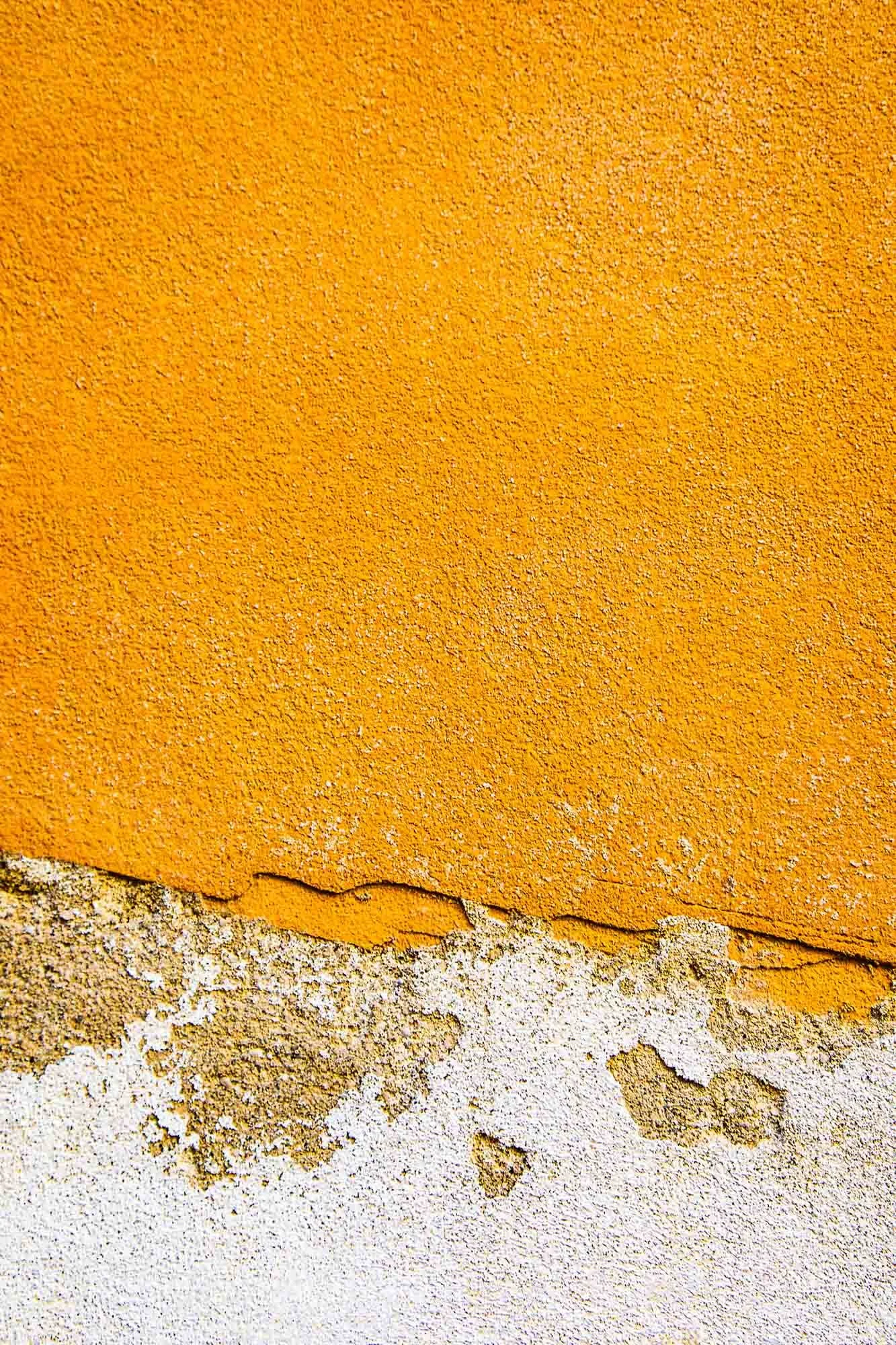 Materiale di muro con uno strato di intonaco arancione sulla parte superiore e uno strato di cemento grigio e bianco sulla parte inferiore, con crepe e screpolature visibili.