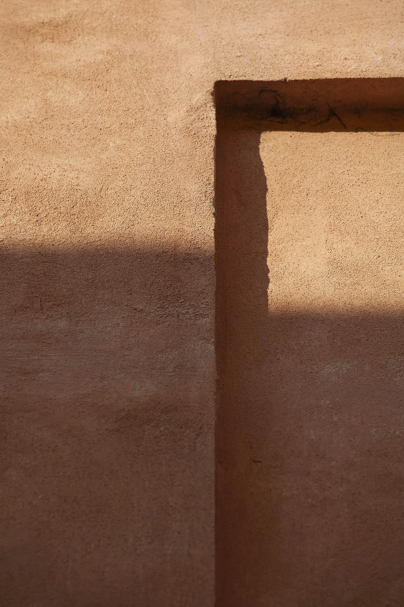 Parete ruvida di colore arancione con un'apertura rettangolare che crea un'ombra sulla superficie.