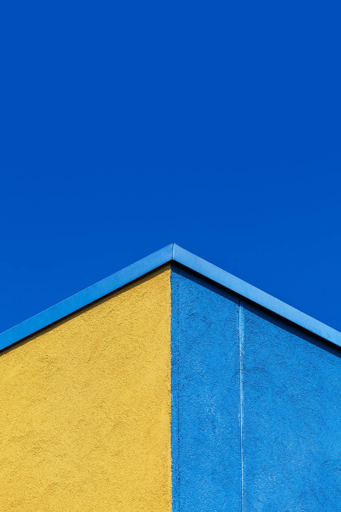 Particolare di un edificio con muro giallo e angolo con muro blu, sopra un cielo azzurro senza nuvole.