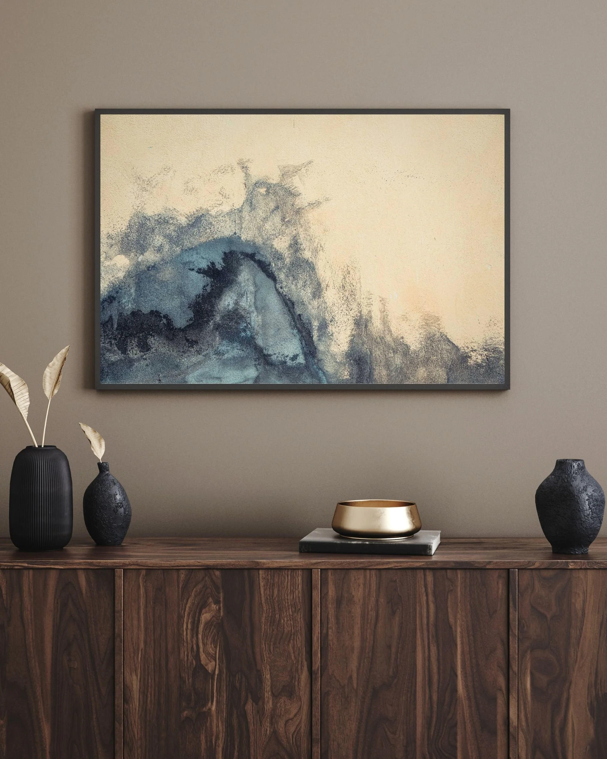 Interno moderno con parete beige, quadro astratto che rappresenta un'onda nei toni del blu e del grigio, al centro tavolo in legno scuro, decorato con vasi neri e una ciotola dorata, con ante in legno naturale.