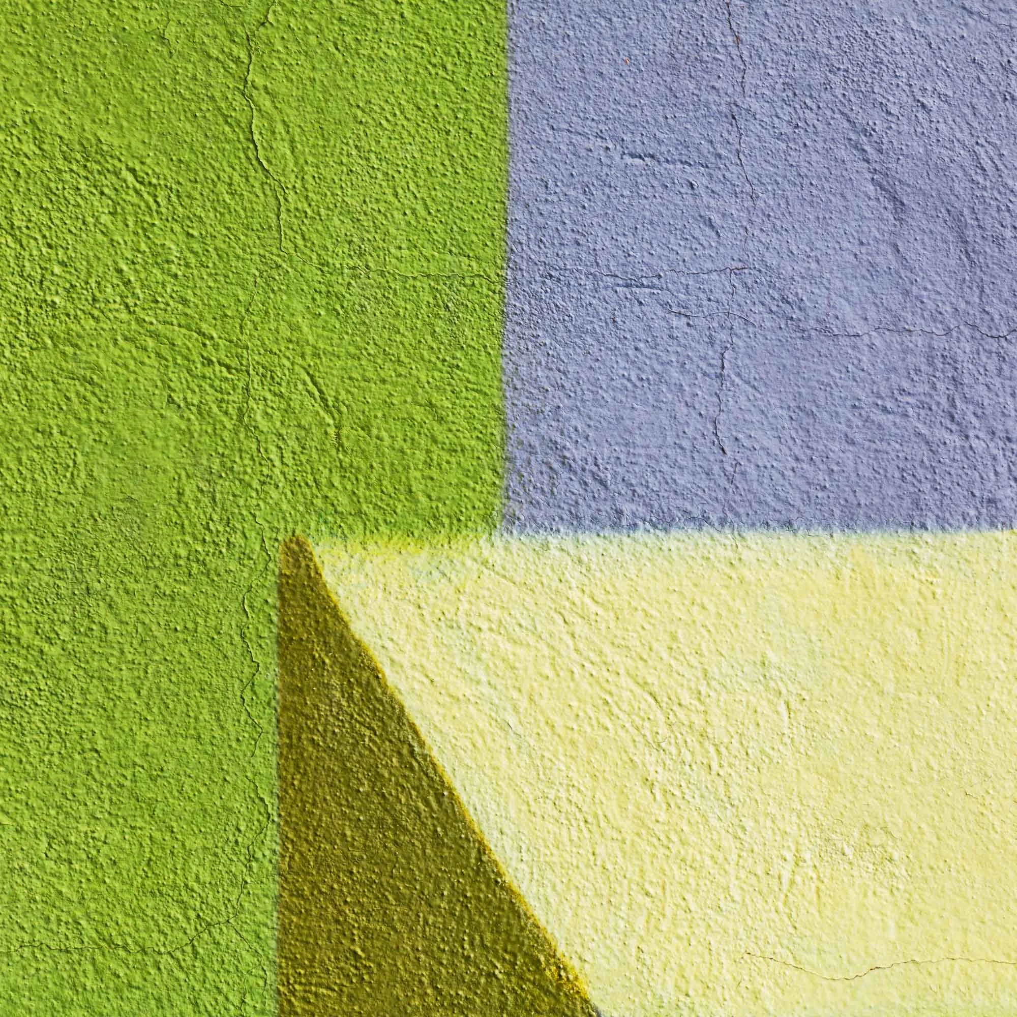 Sezione di un muro dipinto con colori verde, grigio e giallo, con texture e crepe visibili.