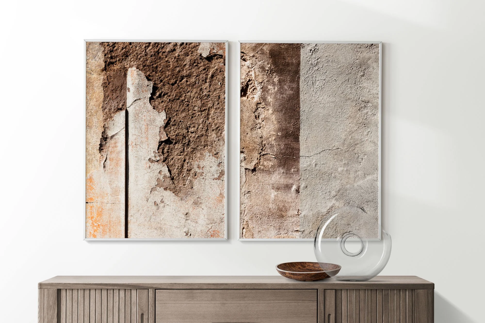 Dipinti di pareti con texture di cemento e pietra appesi su una parete bianca, con sculture di vetro e legno su una credenza in legno chiaro.