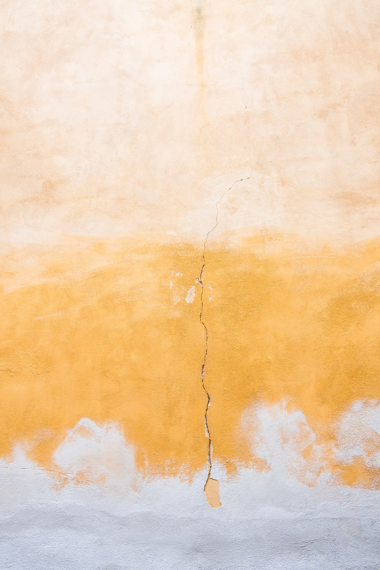 Una parete con muri dipinti con colori caldi, con crepe e zone di scrostamento.