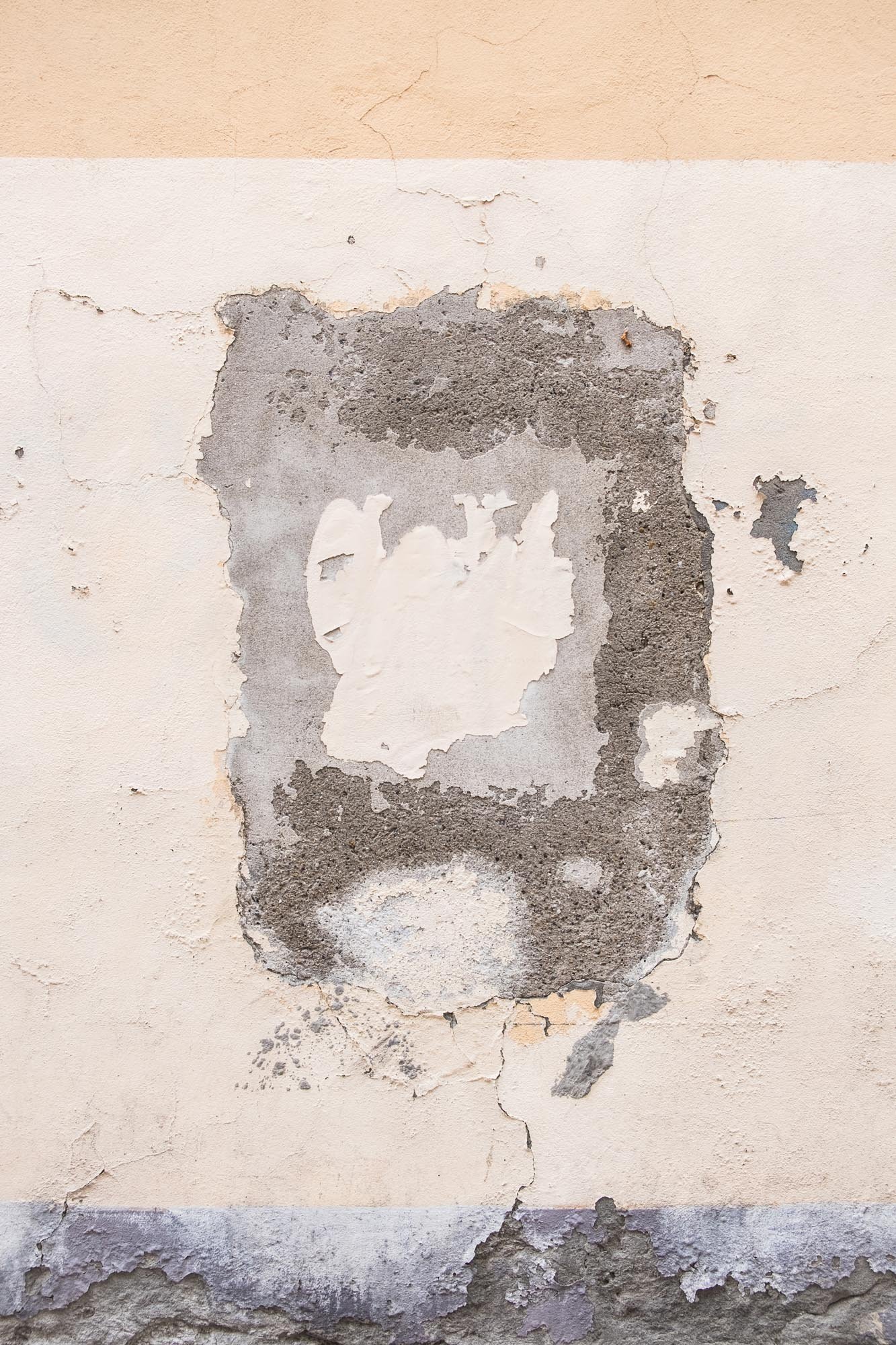 Parete con vernice scrostata e intonaco danneggiato, mostrante strati di pittura e cemento sottostanti.