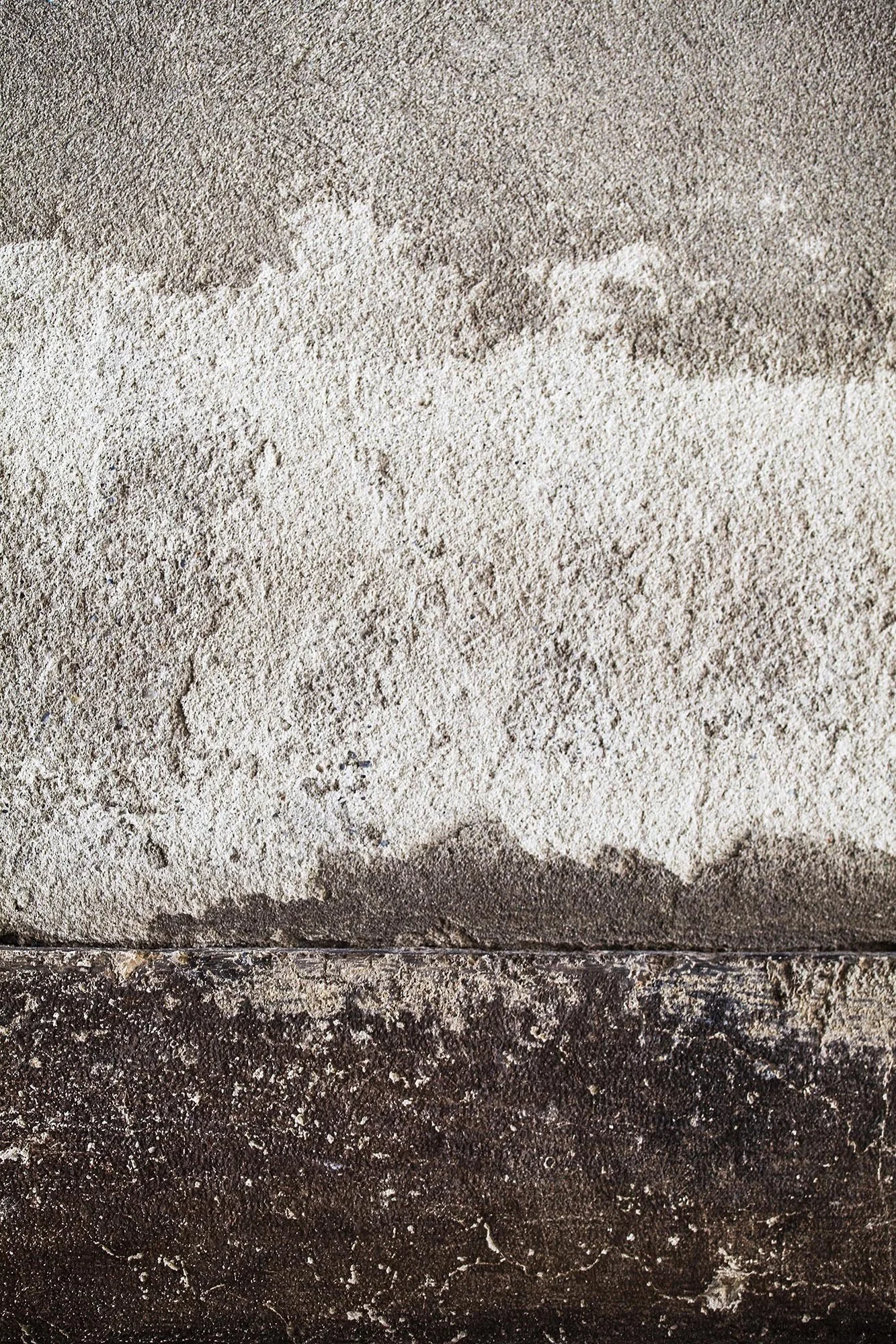 Tre strati di materiali con diversa colorazione e consistenza, dal chiaro al scuro, con una base di pietra o cemento.
