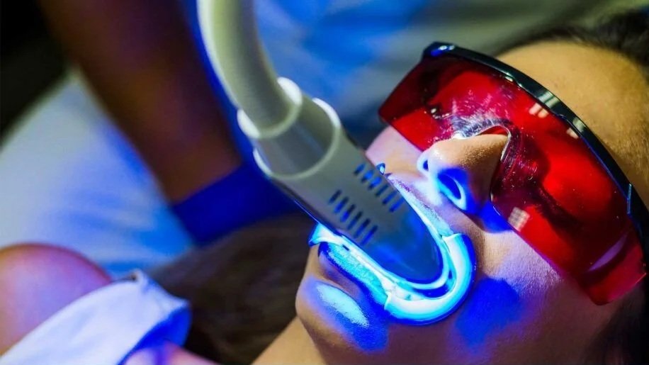 Person wearing red protective glasses receiving dental treatment with a blue light during a dental procedure.