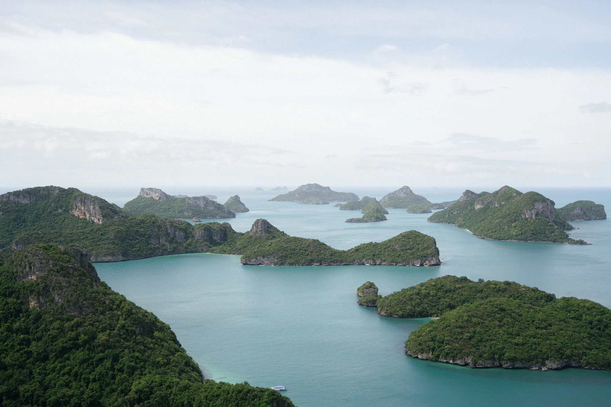 Aerial view of lush green islands and limestone karsts in a turquoise bay under overcast sky.