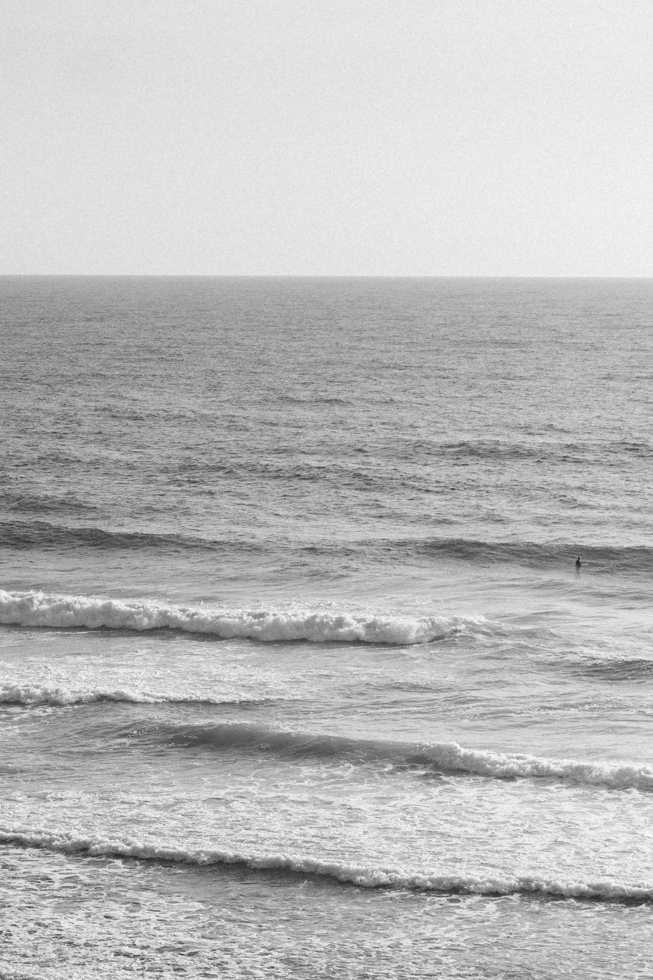 Black and white photo of ocean waves with a lone person standing in the water