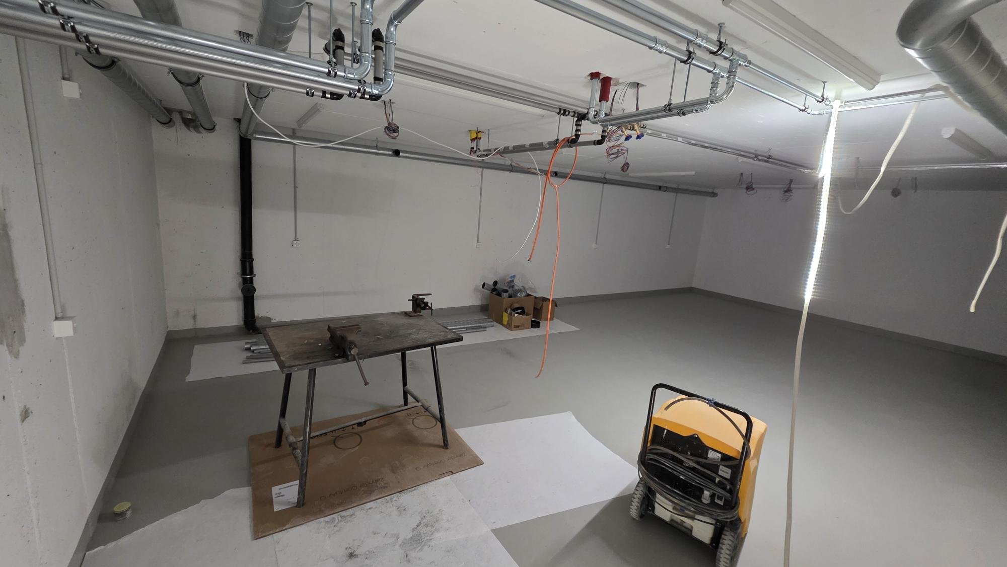 Innenraum einer Baustelle mit Rohrleitungen an der Decke, Werkbank, Werkzeugkoffer, Kabel und Bauausrüstung.
