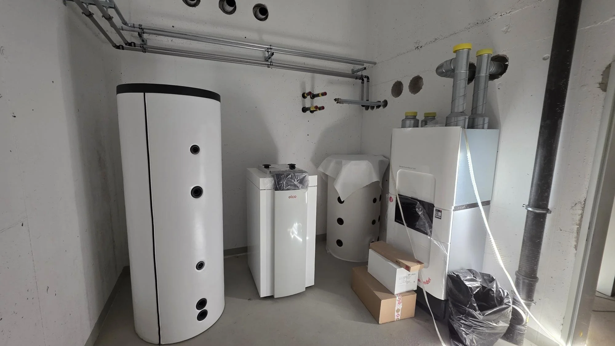 Ein Raum mit Wasserboiler, Heizungen, Rohren und Installationsteilen, vermutlich ein Hauswirtschaftsraum oder Technikraum