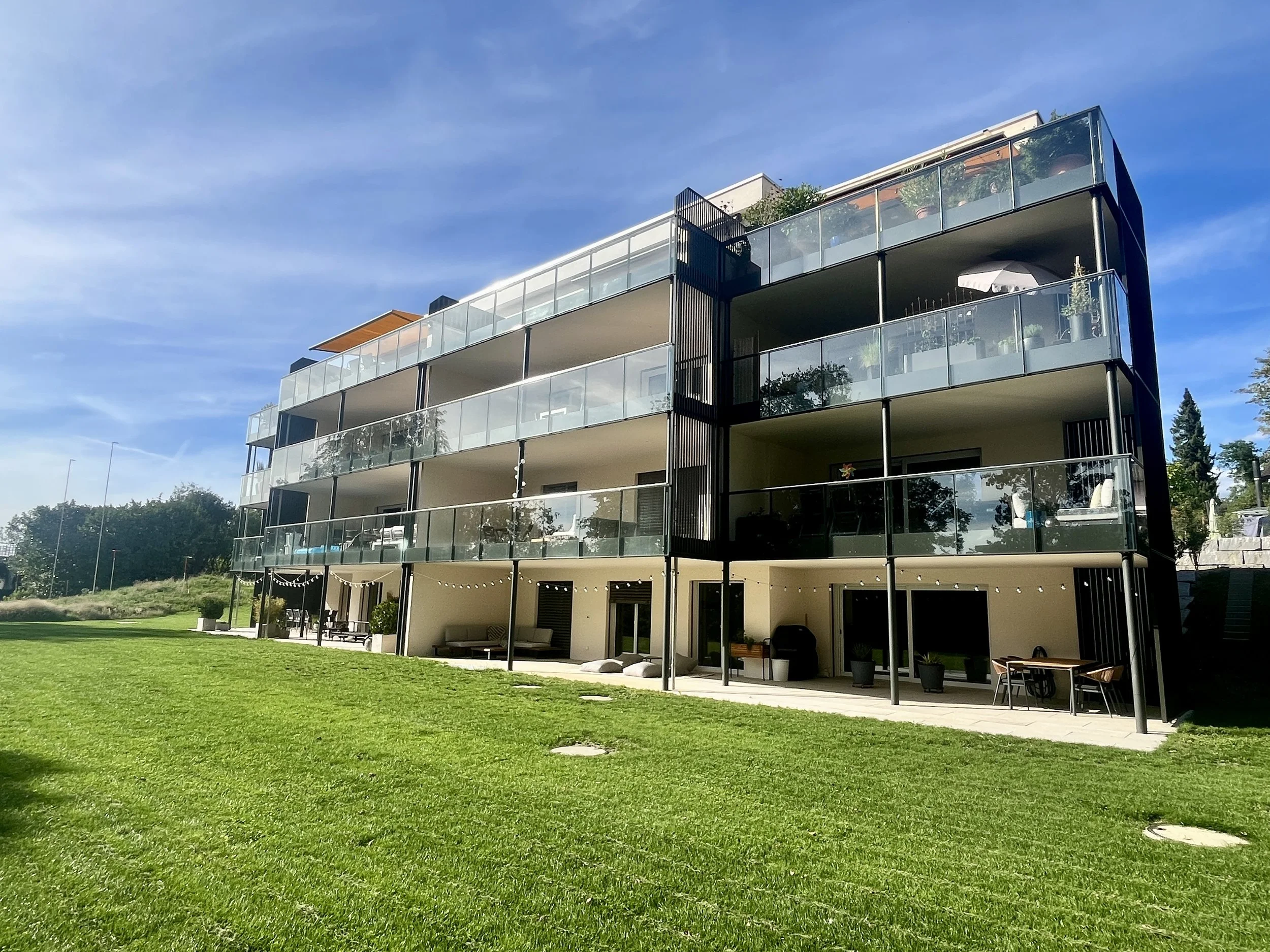 Modernes Mehrfamilienhaus am Bergliweg in Frauenfeld mit grossen Balkonen, viel Grünfläche und einem klaren blauen Himmel.