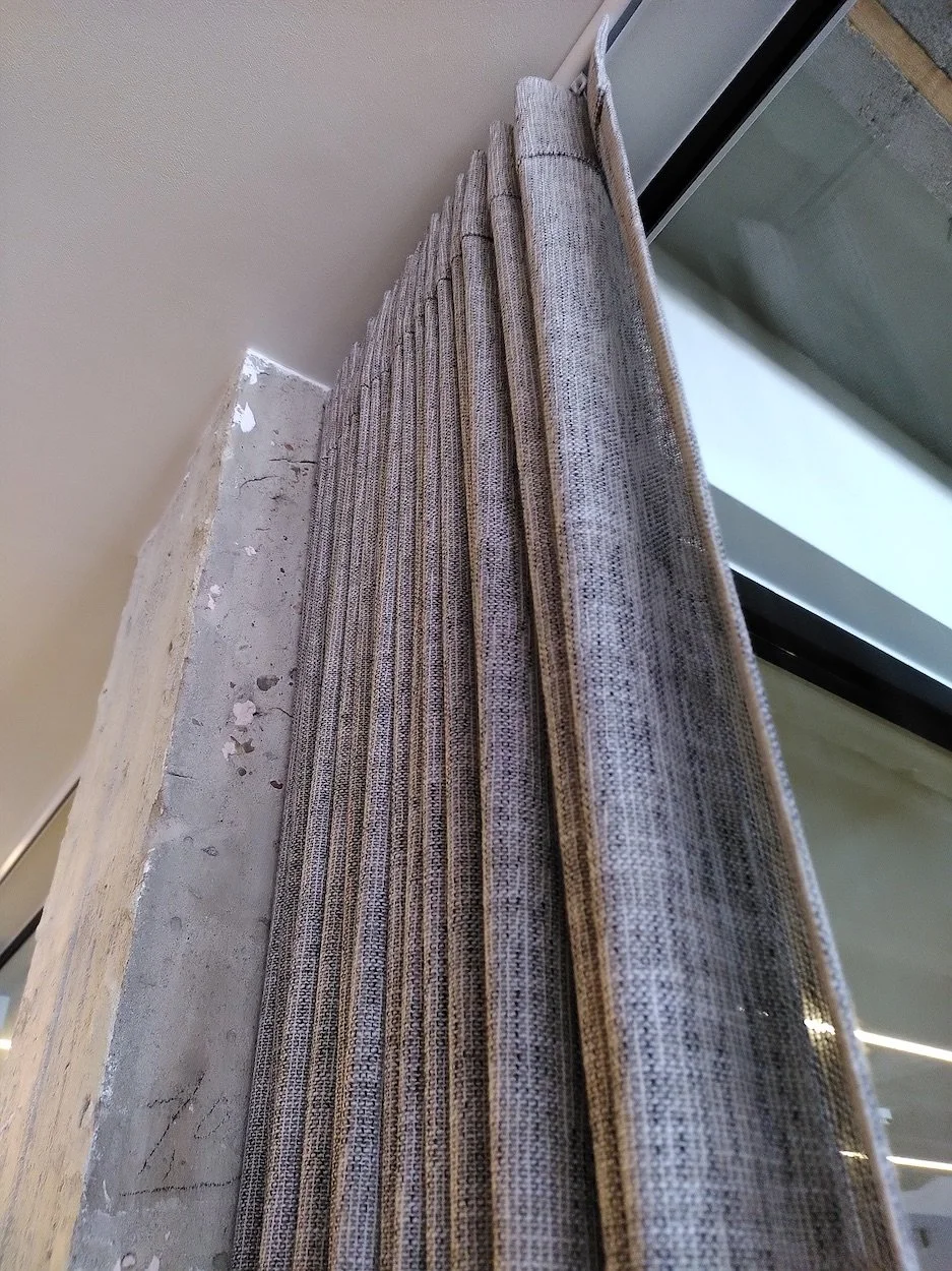 Gordijnen die vlak naast een glazen deur hangen, met een betonnen muur ernaast.