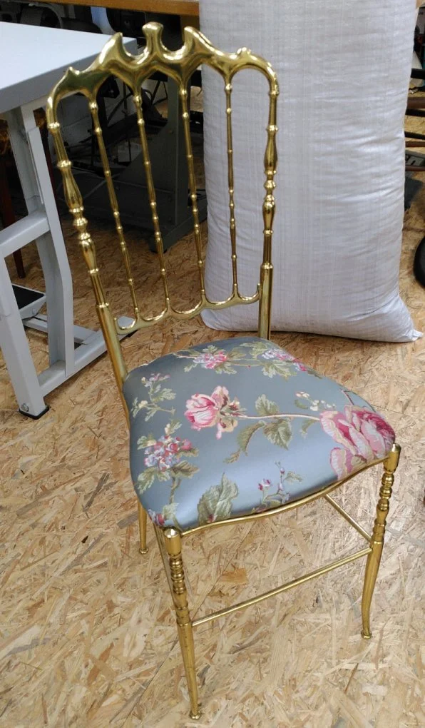 Een goudkleurige metalen stoel met een fleurige fleurige bekleding op een houten vloer. Dit is het resultaat van een van de deelnemers aan een Open Atelier Workshop bij Katrijn De Waele.