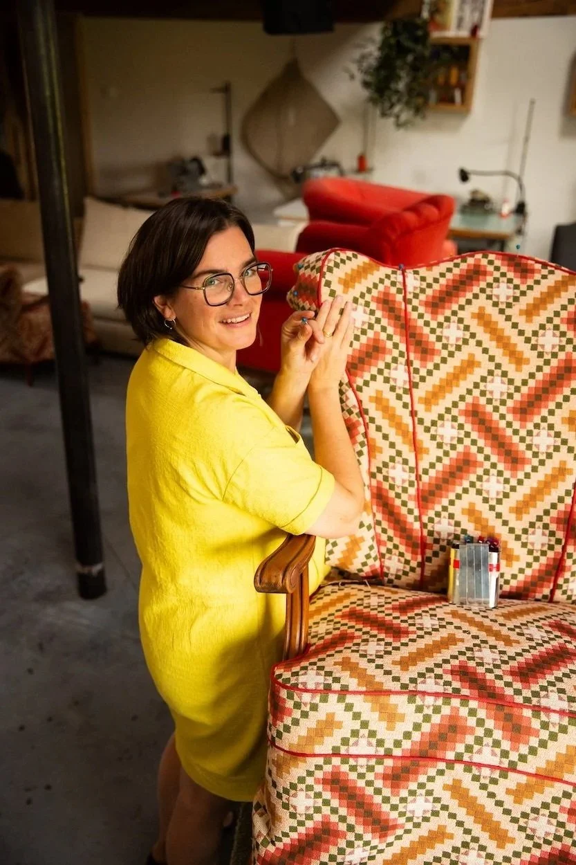 Vrouw in gele jurk - Katrijn De Waele - is bezig aan het herstofferen van een antieke houten stoel.