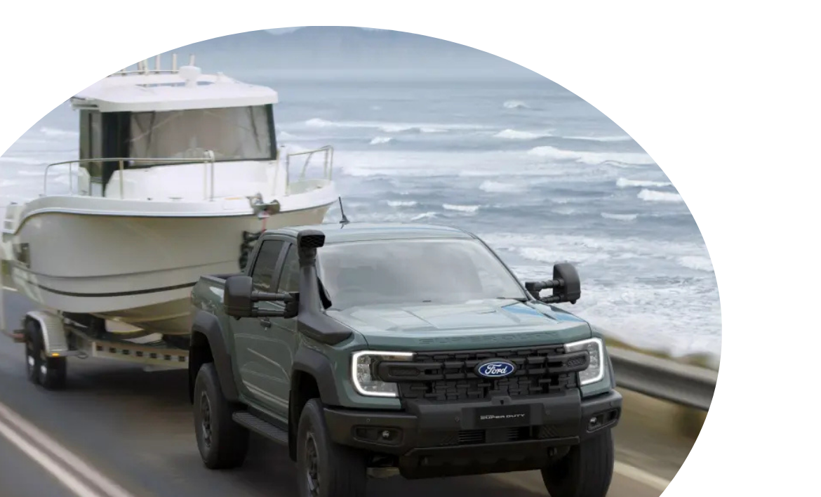 Black Ford pickup truck towing a boat on a trailer along a coastal highway.