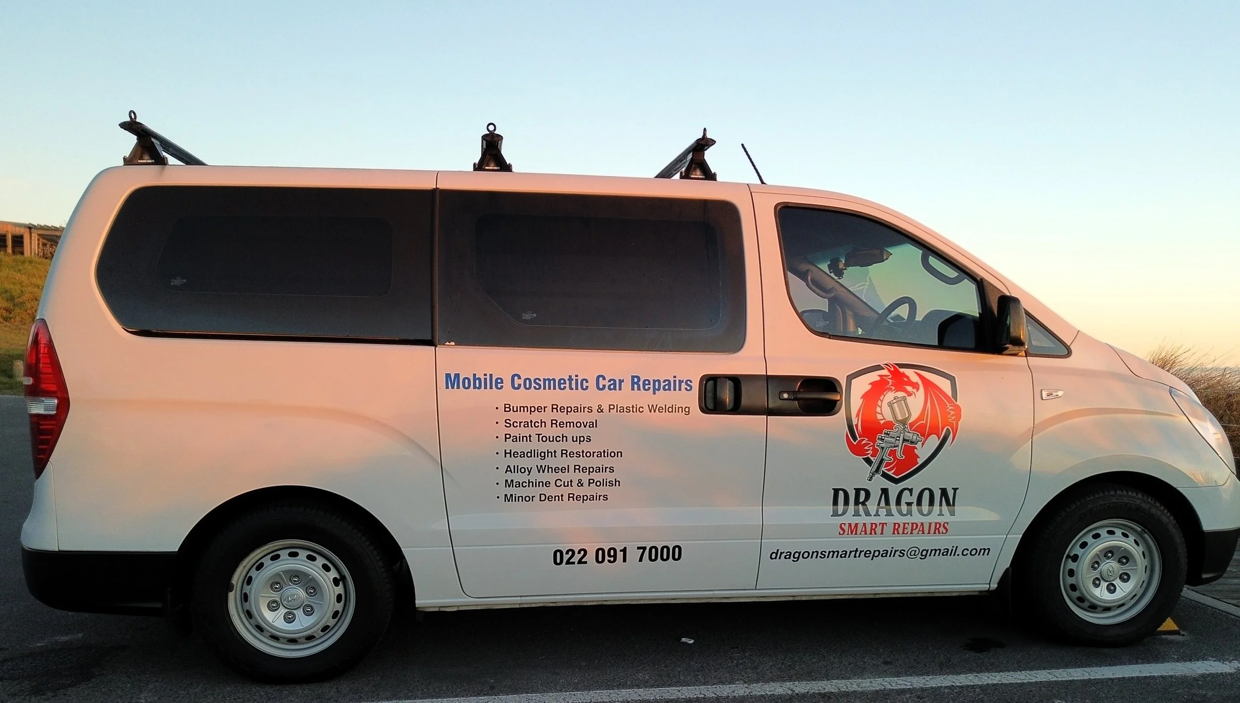 A white commercial van with the company name 'Dragon Smart Repairs' and a dragon logo on the side. The van displays services offered such as bumper repairs, scratch removal, and paint touch-ups.