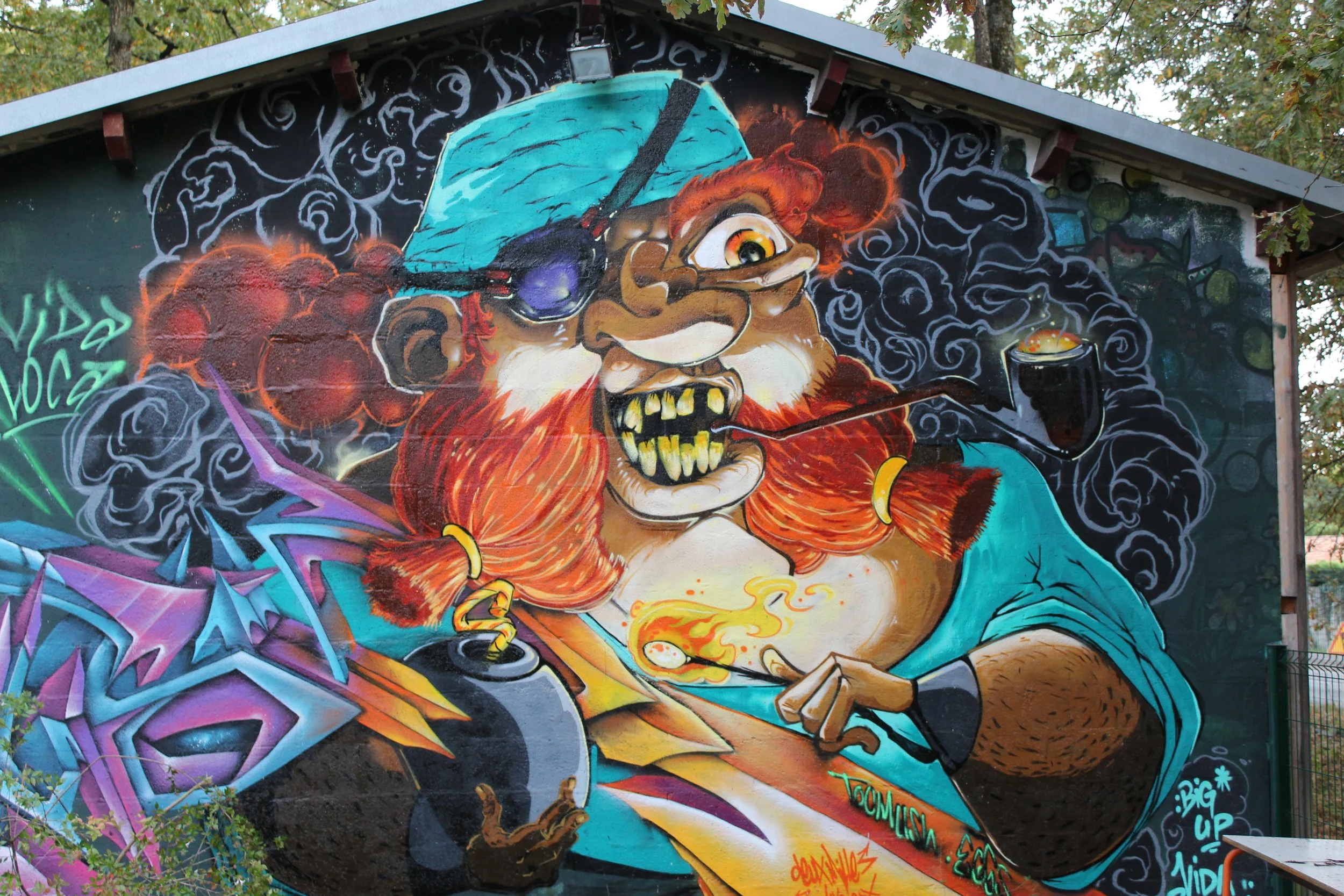 Graffiti représentant un personnage fantastique avec une peau rouge, des yeux jaunes, des dents pointues, portant un casque de chantier bleu, et fumant une pipe, avec un fond coloré de nuages noirs et de formes abstraites.