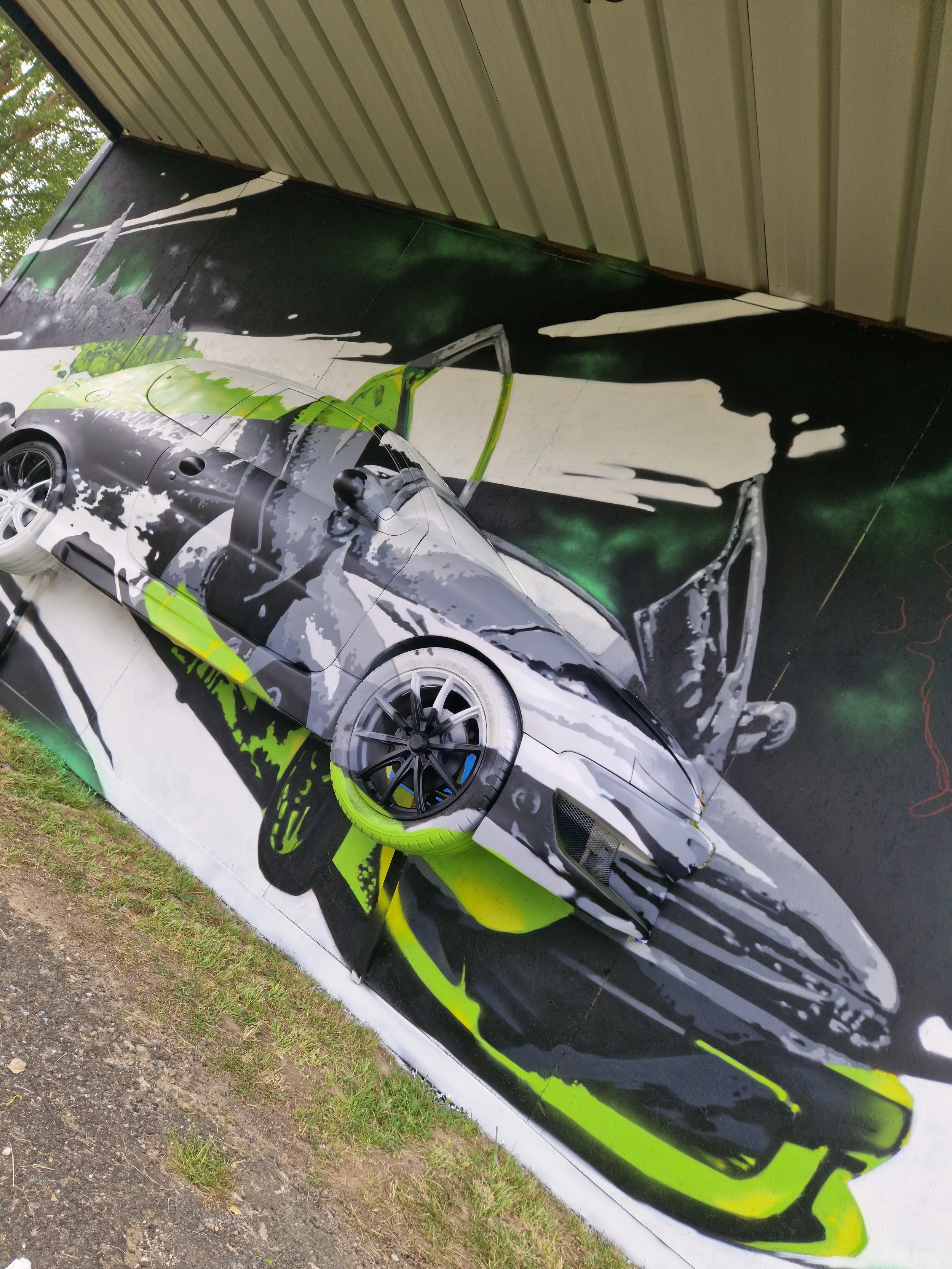 Une œuvre d'art murale représentant une voiture de sport stylisée avec des couleurs noir, blanc, gris et vert fluorescent, peinte sur un panneau extérieur sous un toit en métal.