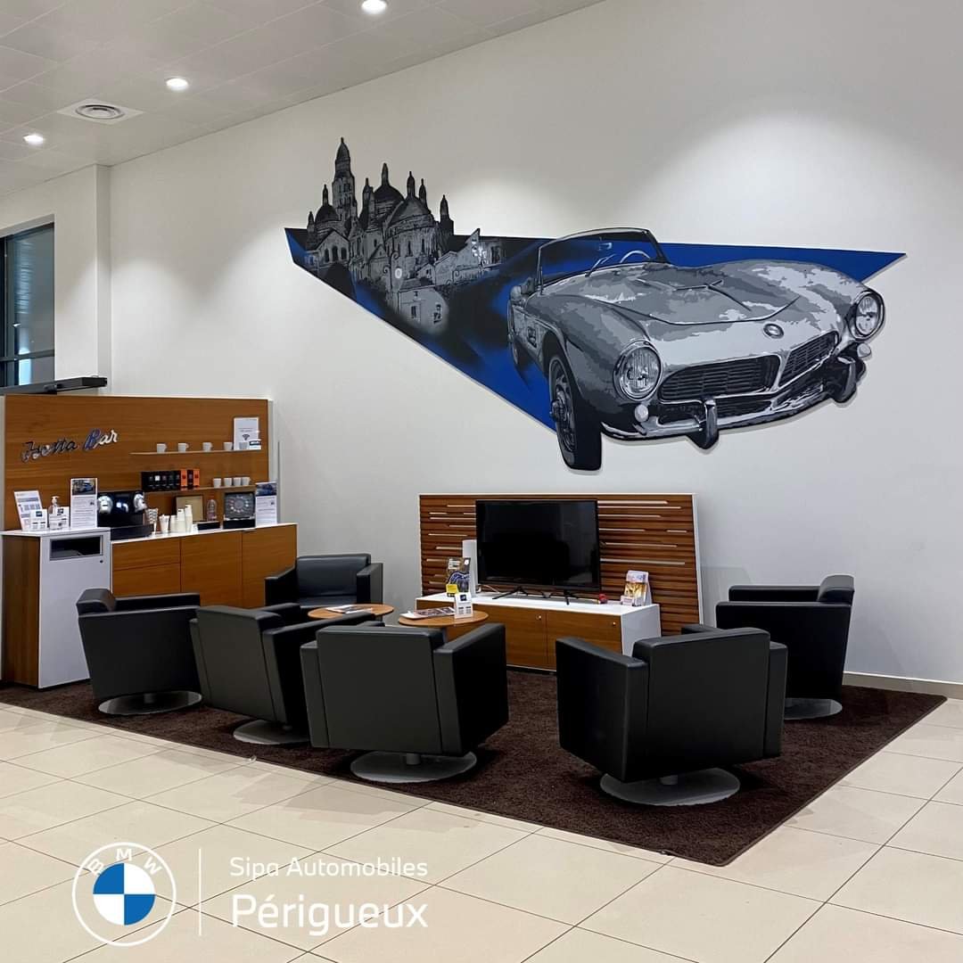 Salon d'accueil avec une peinture murale représentant une voiture classique et un château, meubles noirs, écran de télévision, ambiance moderne et élégante.
