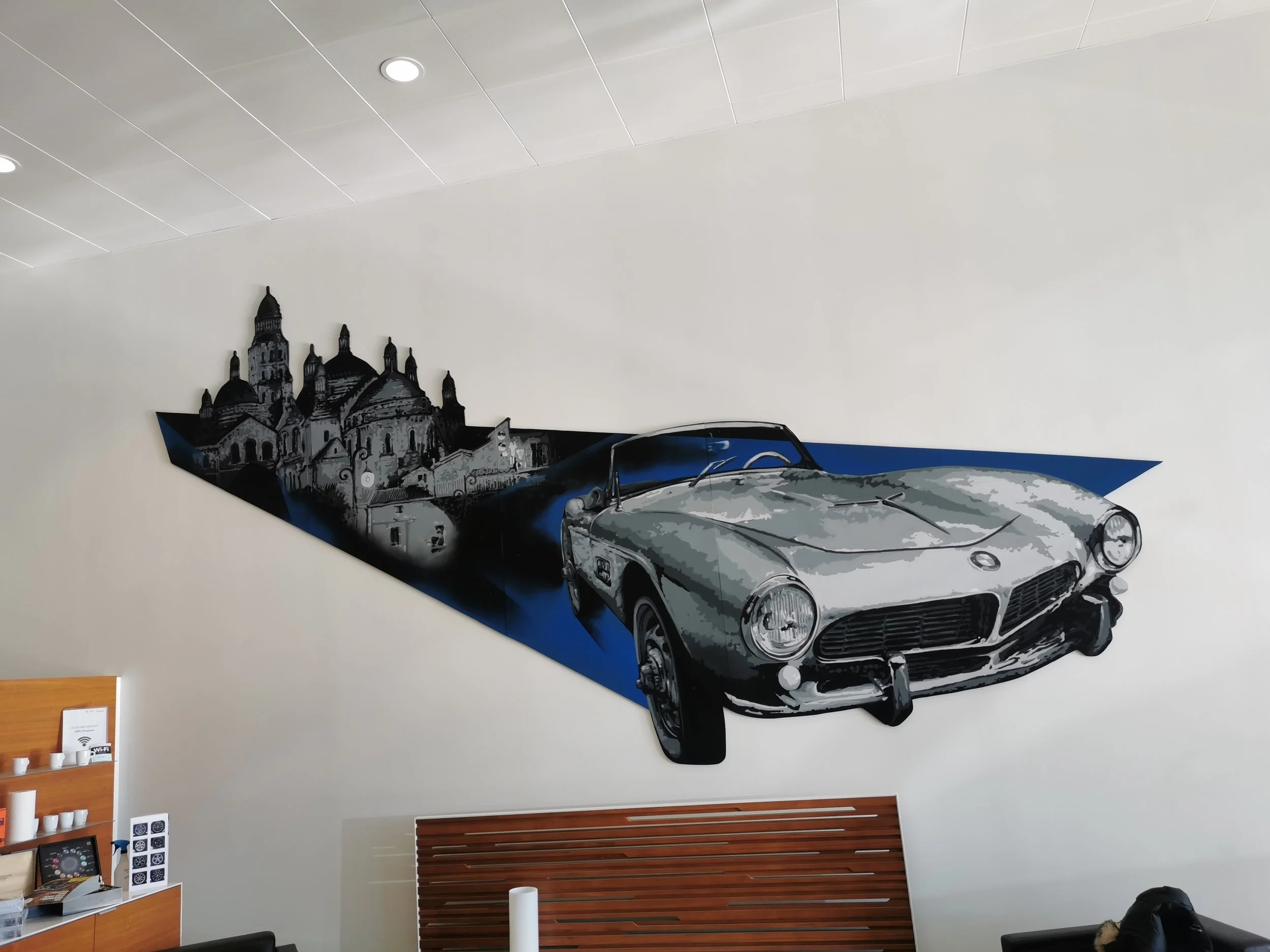 Mur avec une peinture murale d'une voiture de course et d'un bâtiment historique en arrière-plan, dans un intérieur moderne.