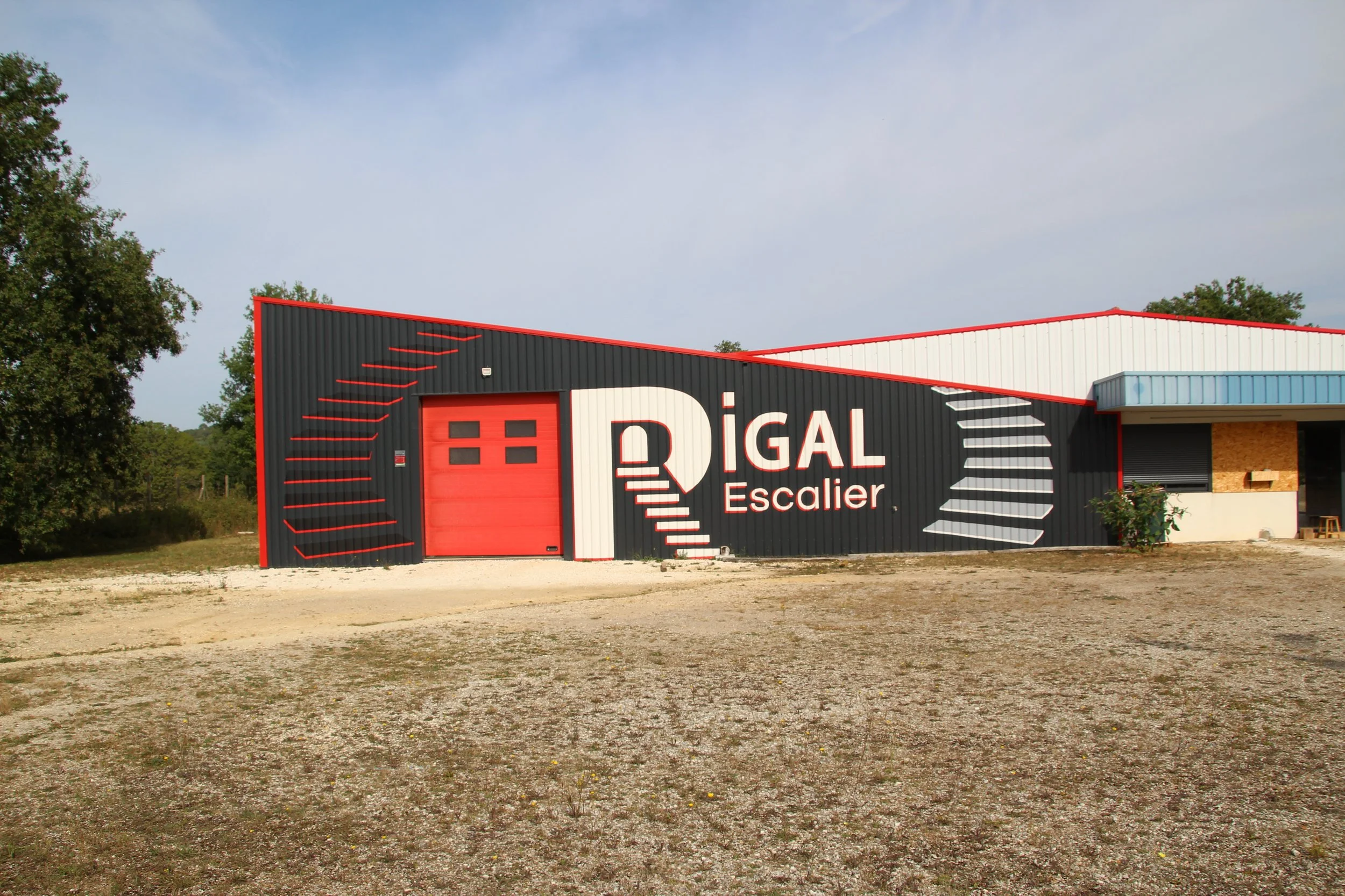 Façade d'un bâtiment avec une porte de garage rouge et un panneau avec le mot 'RIGAL Escalier' en blanc sur fond noir, entouré d'éléments graphiques rouges et blancs, le tout sous un ciel clair et avec des arbres en arrière-plan.