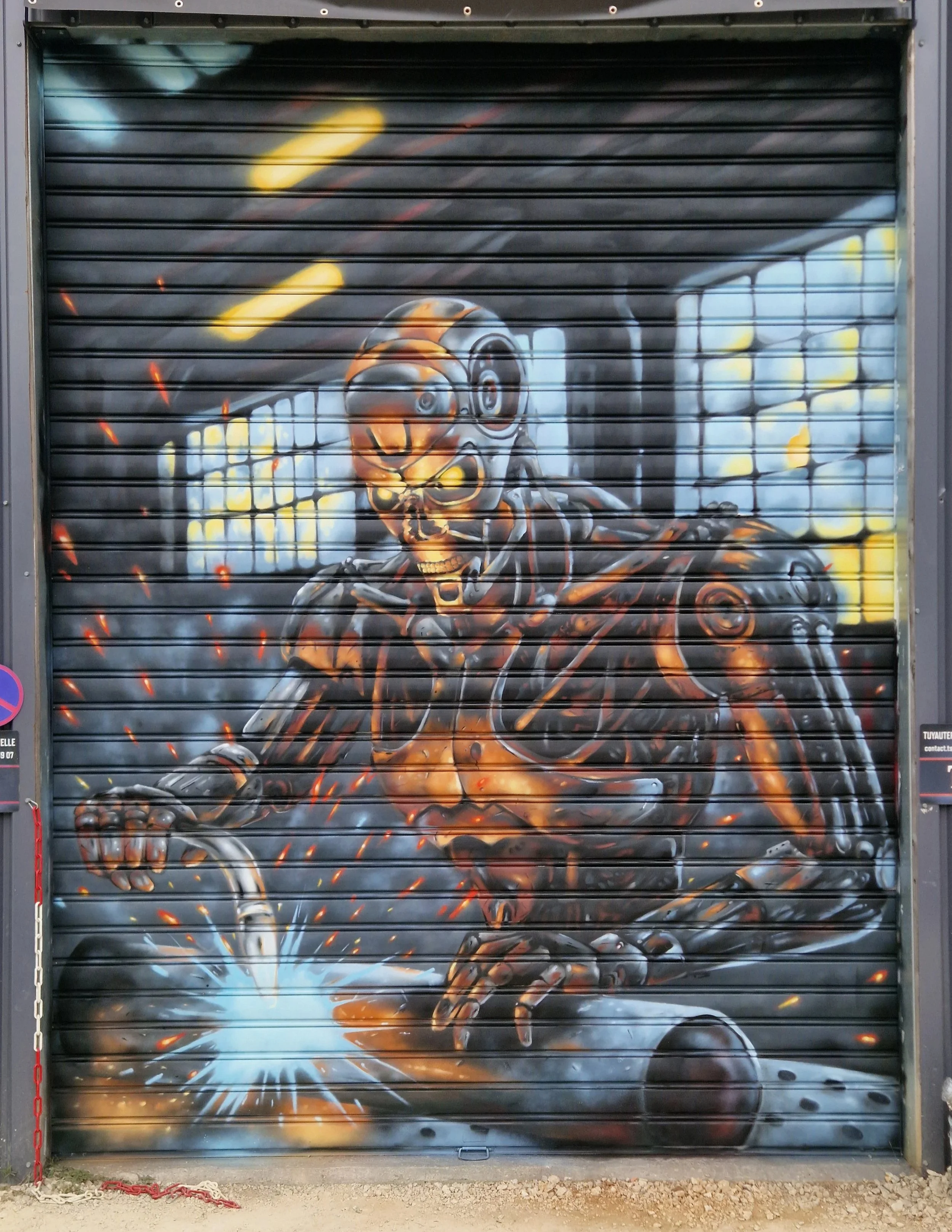 Peinture murale de style street art représentant un squelette avec casque de moto, lunettes, et une moto, avec des effets de lumière et d'étincelles, sur une porte métallique de magasin.