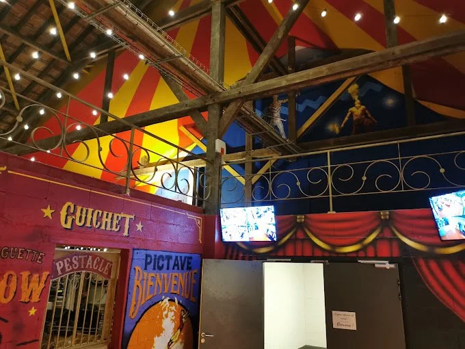 Intérieur d'une attraction de cirque, avec une scène décorative, des écrans, et des panneaux en français avec des textes comme 'Gughet', 'Pestacle', et 'Pictave Bienvenue'.