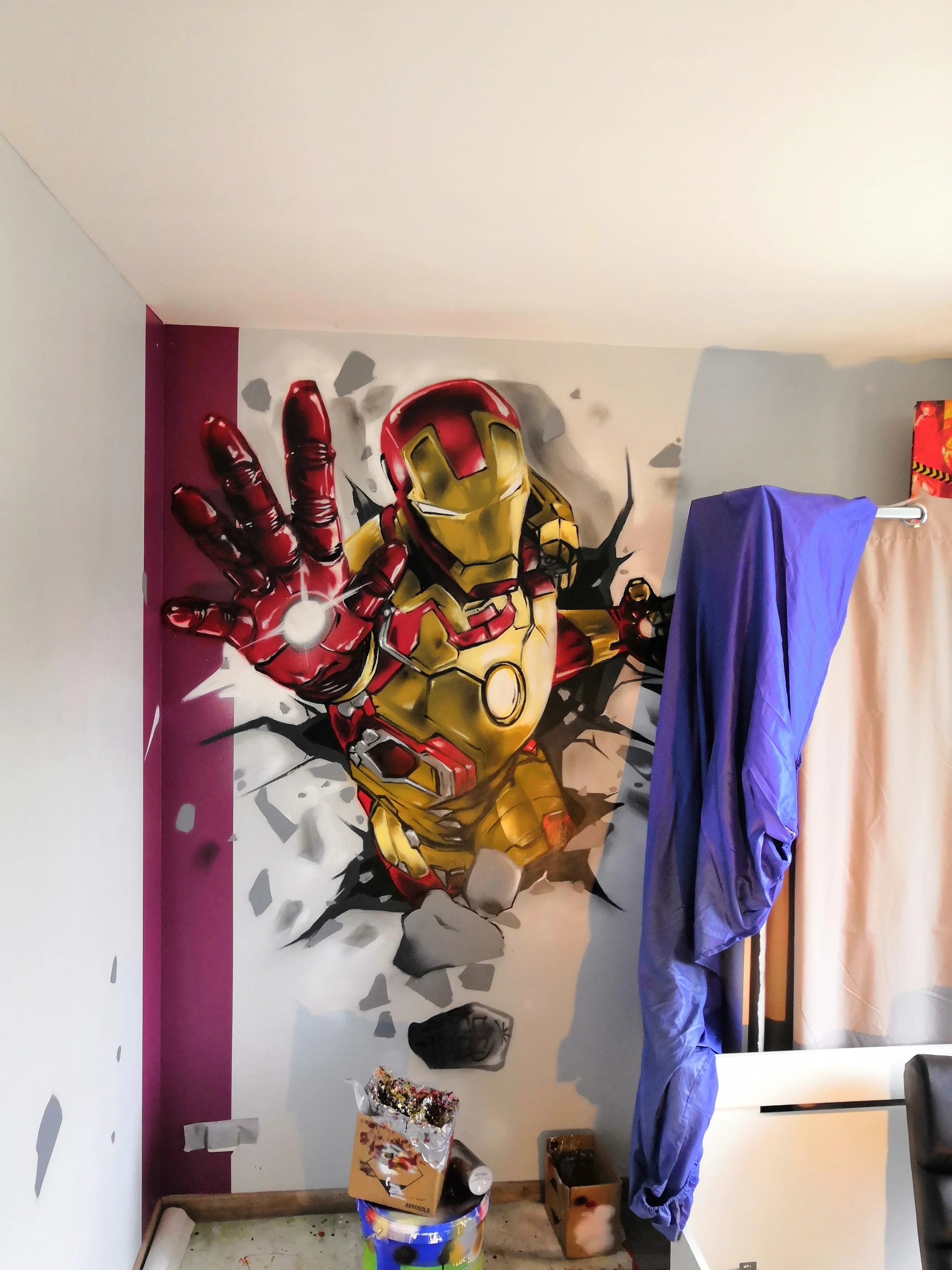 Mur avec un poster d'Iron Man en train de lancer un poing, entouré de débris et de peinture éclatée, avec des draps de protection suspendus devant.