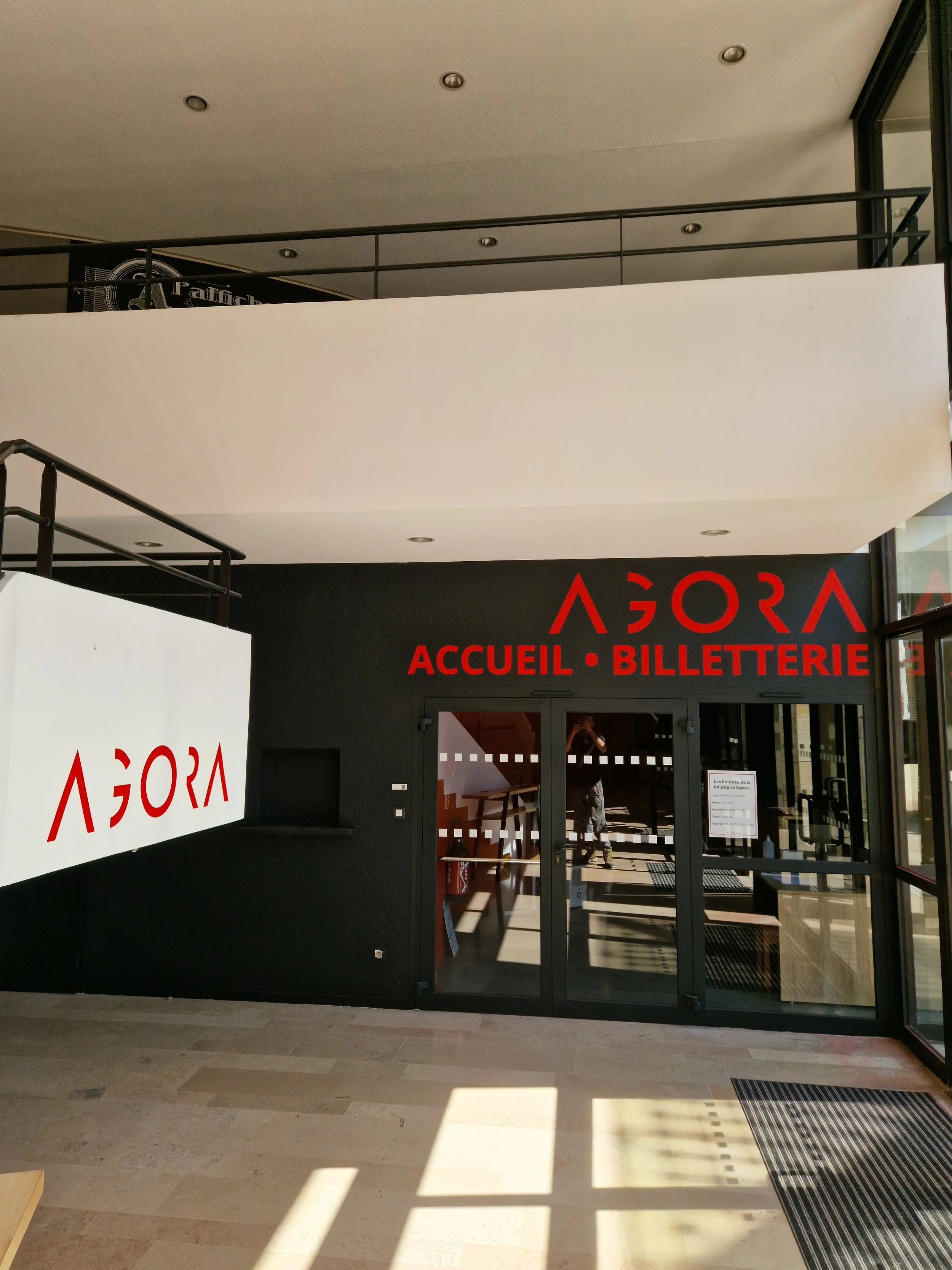 Entrée d'un bâtiment avec une porte en verre et un panneau indiquant 'Accueil Billetterie' en rouge sur un fond noir.