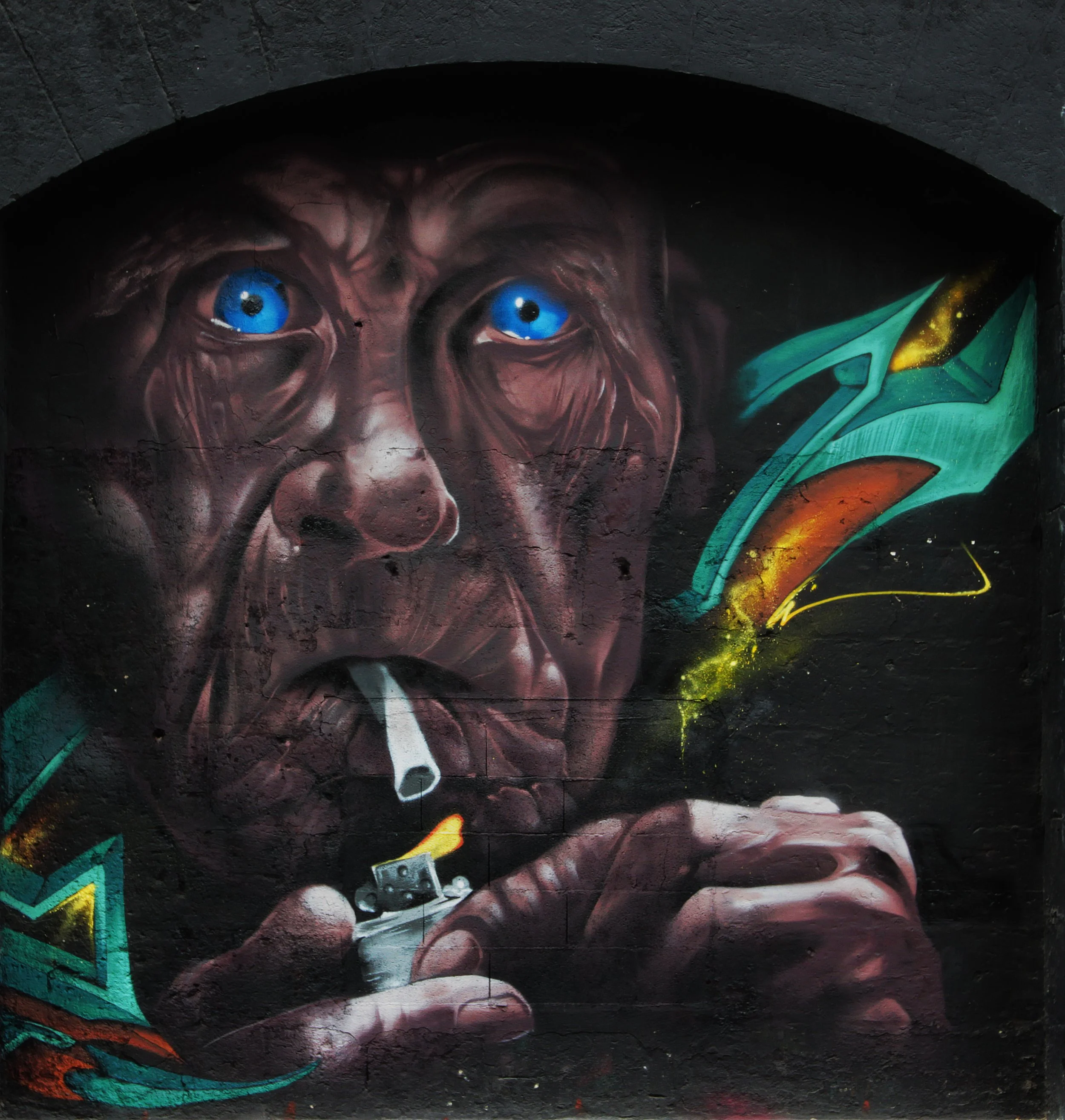 Graffiti représentant un visage humain avec des yeux bleus et des détails colorés, notamment une aile verte à droite.