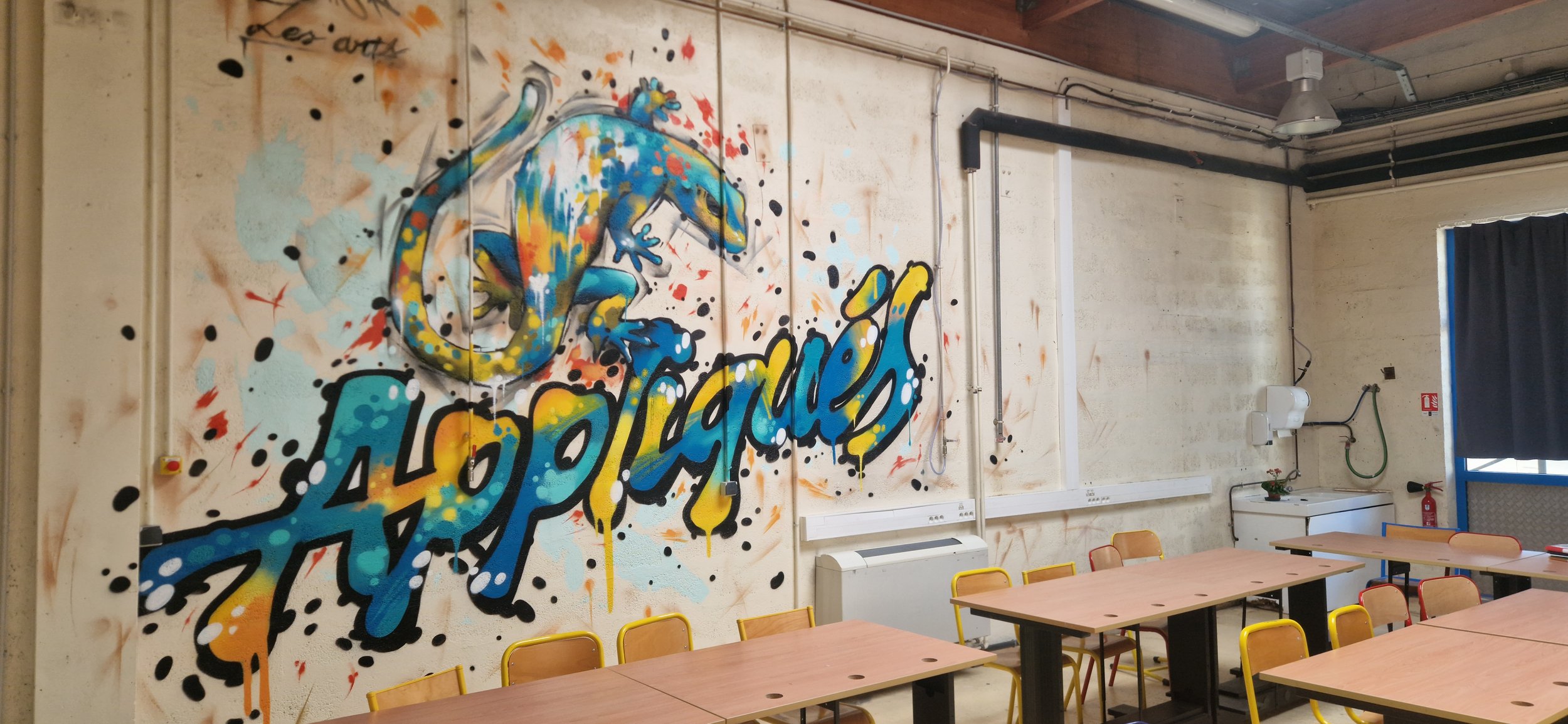 graffiti coloré représentant un lézard et le mot 'appliqués' dans une salle de classe avec tables et chaises. Réalisation collective au sein du lycée pro Léonard de Vinci.