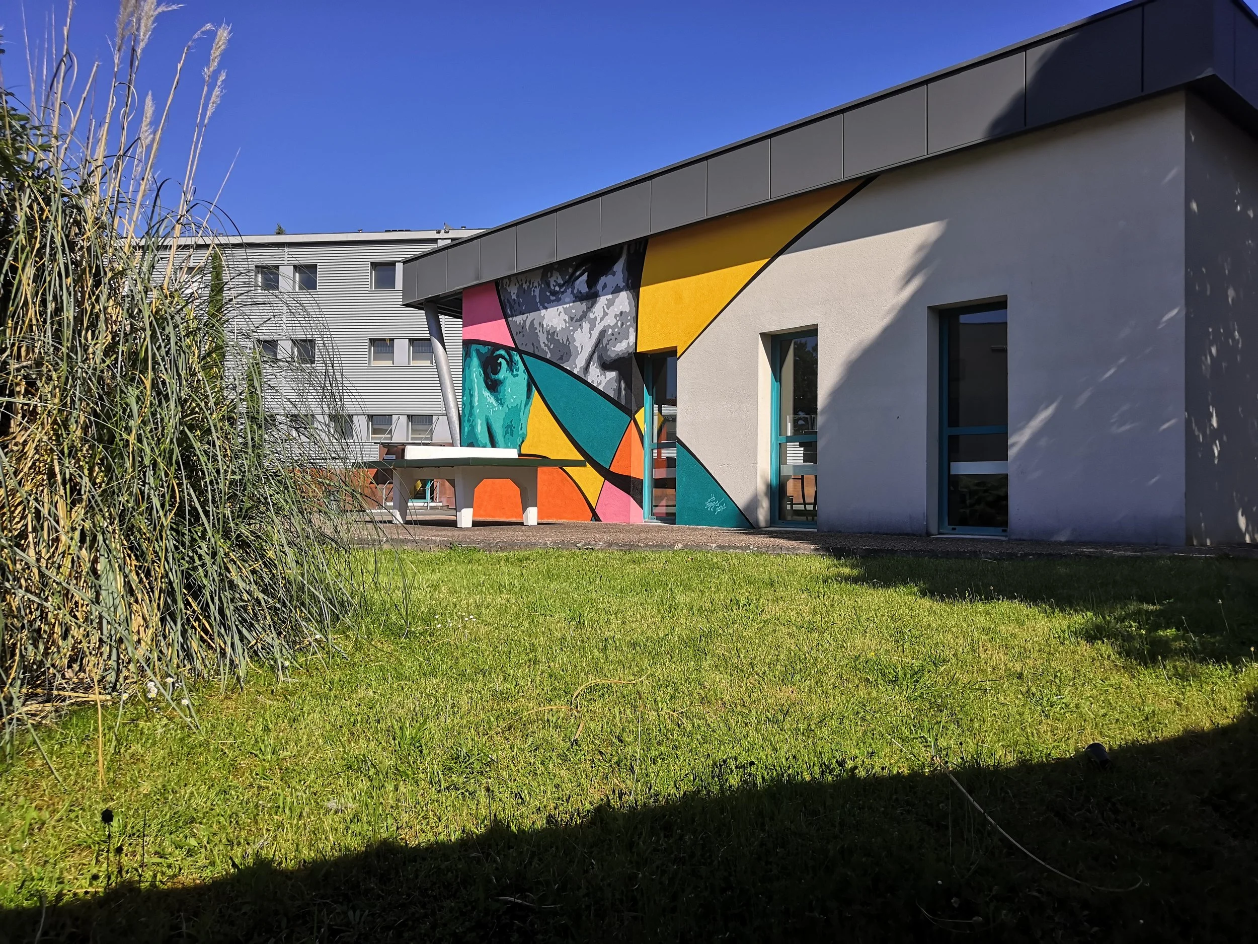 Un bâtiment moderne avec un mur peint d'une fresque colorée représentant une femme africaine avec un style artistique abstrait, sous un ciel bleu clair. réalisé par EGGS EGGS58STUDIO