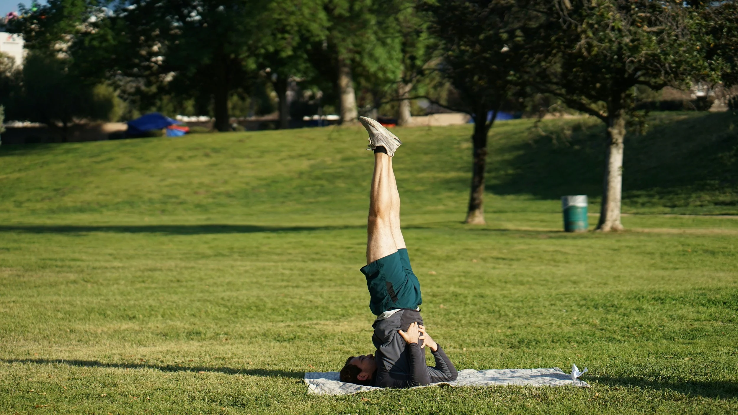 A person practicing yoga outdoors on a grassy field, lying on their back with their legs raised straight up in the air.