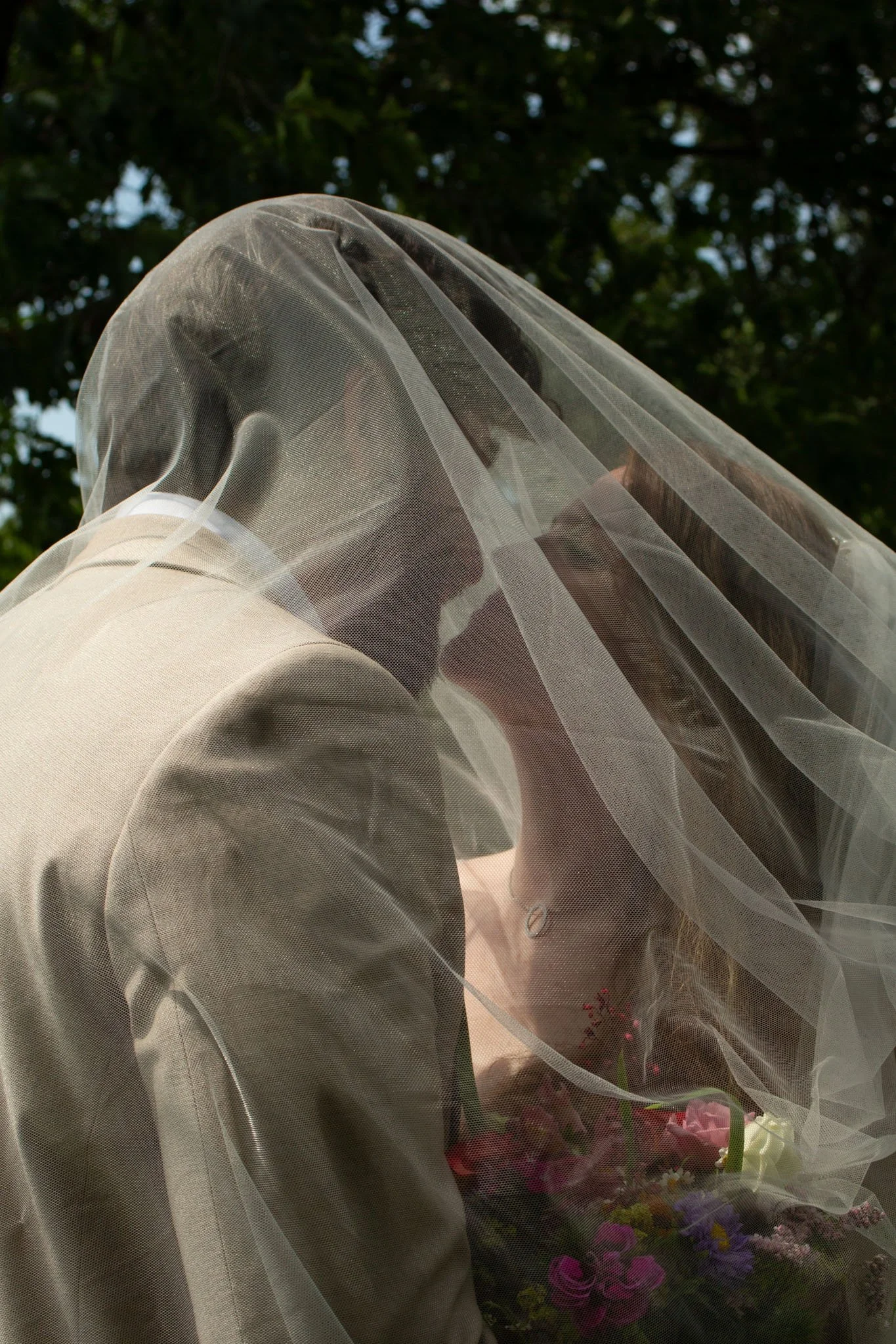 Braut mit Schleier und Brautstrauß, fotografiert durch den zarten Tüllschleier – detailreiche und emotionale Hochzeitsfotografie.