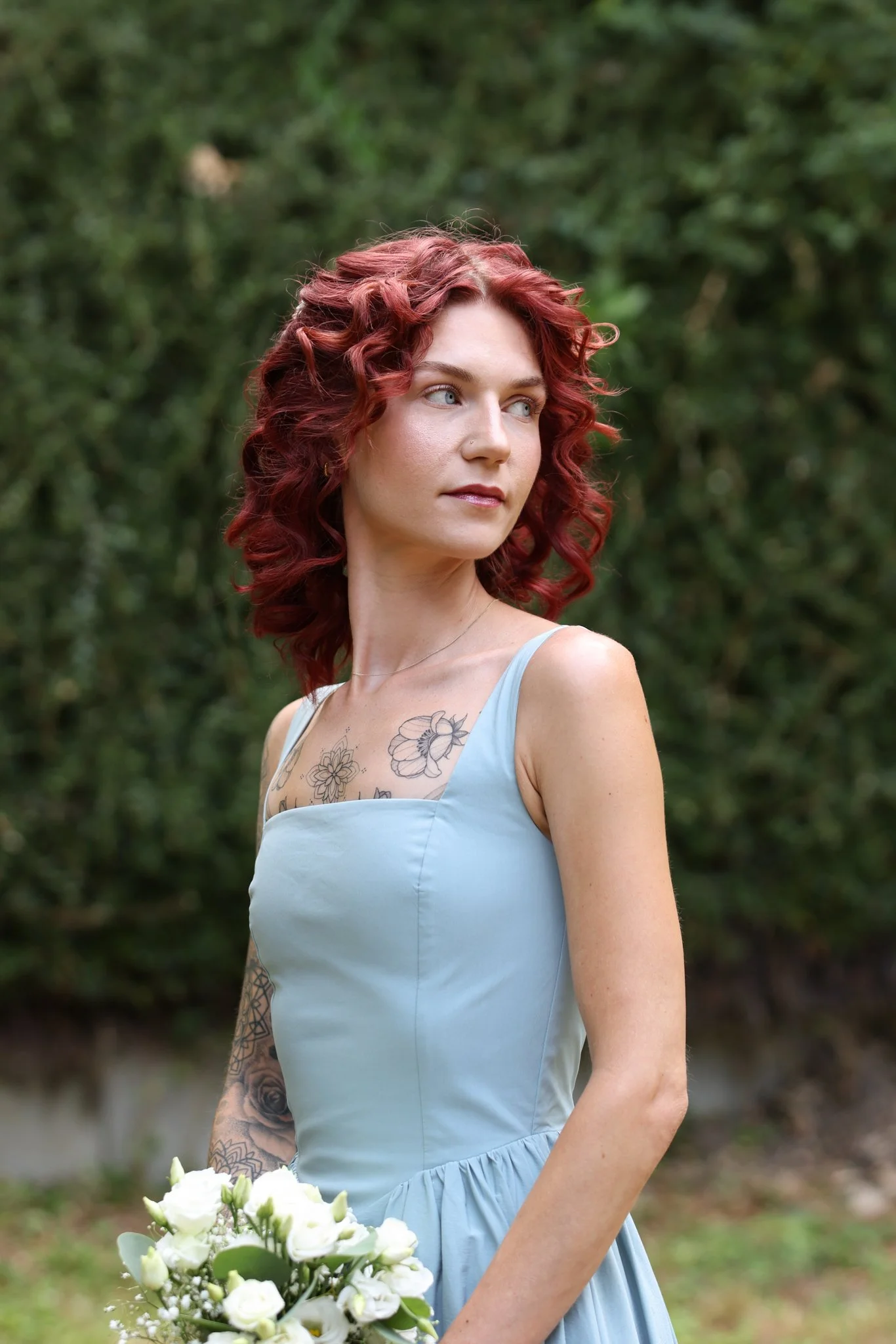 Brautjungfer im hellblauen Kleid mit weißem Blumenstrauß in natürlicher Umgebung.