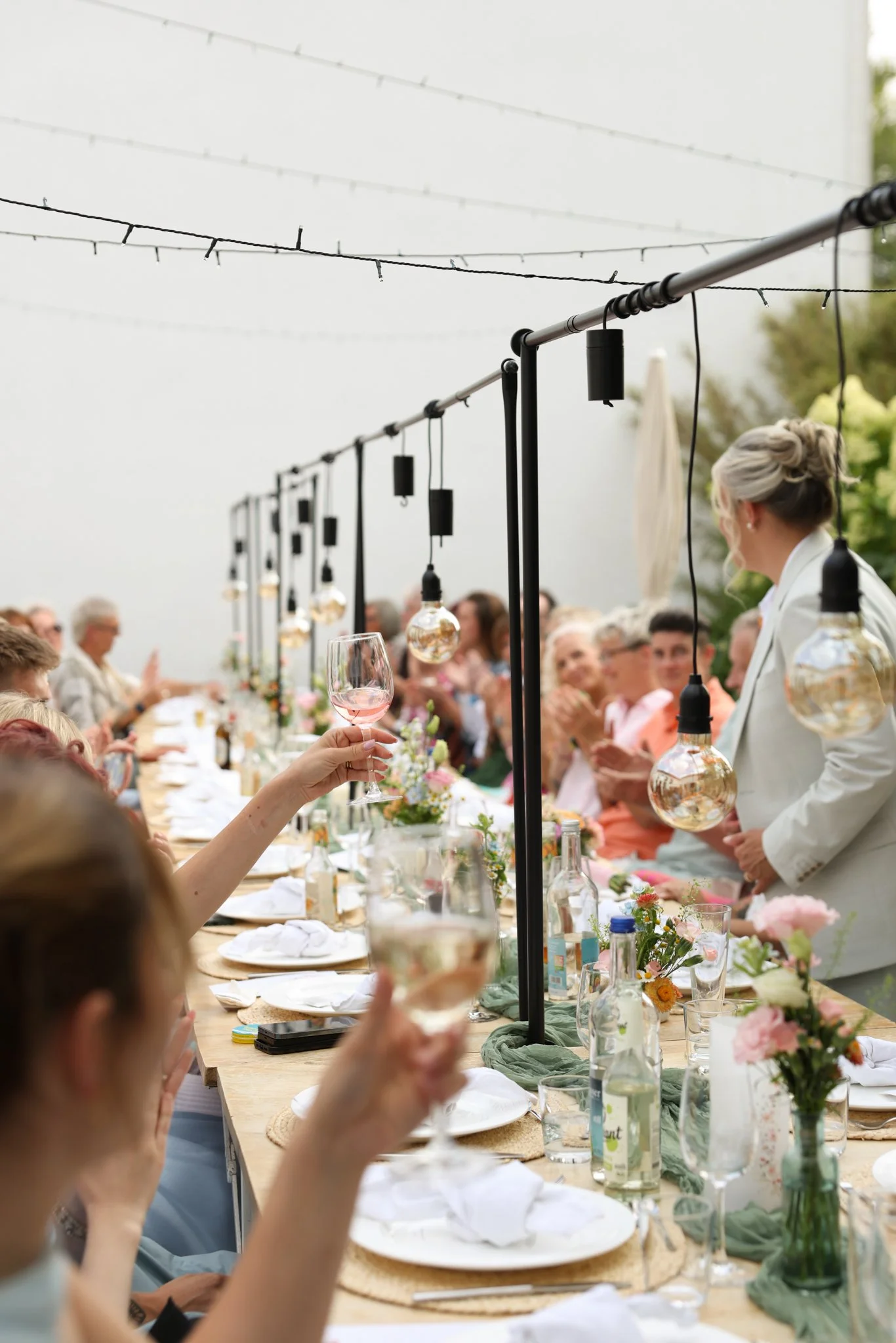 Festlich gedeckter Tisch unter freiem Himmel mit Blumendekoration und Lichterketten während einer Hochzeitsfeier.