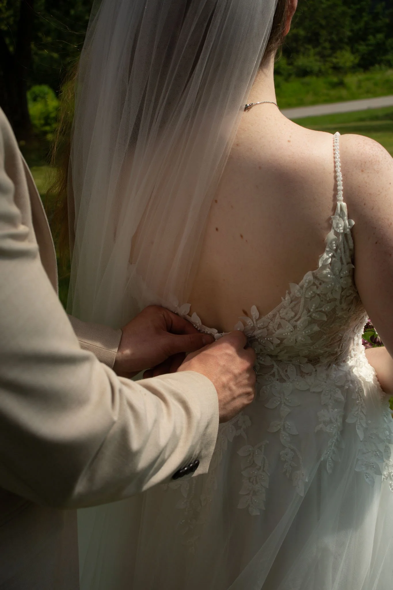 Nahaufnahme des Brautkleids, während die Knopfleiste vor der Trauung geschlossen wird.